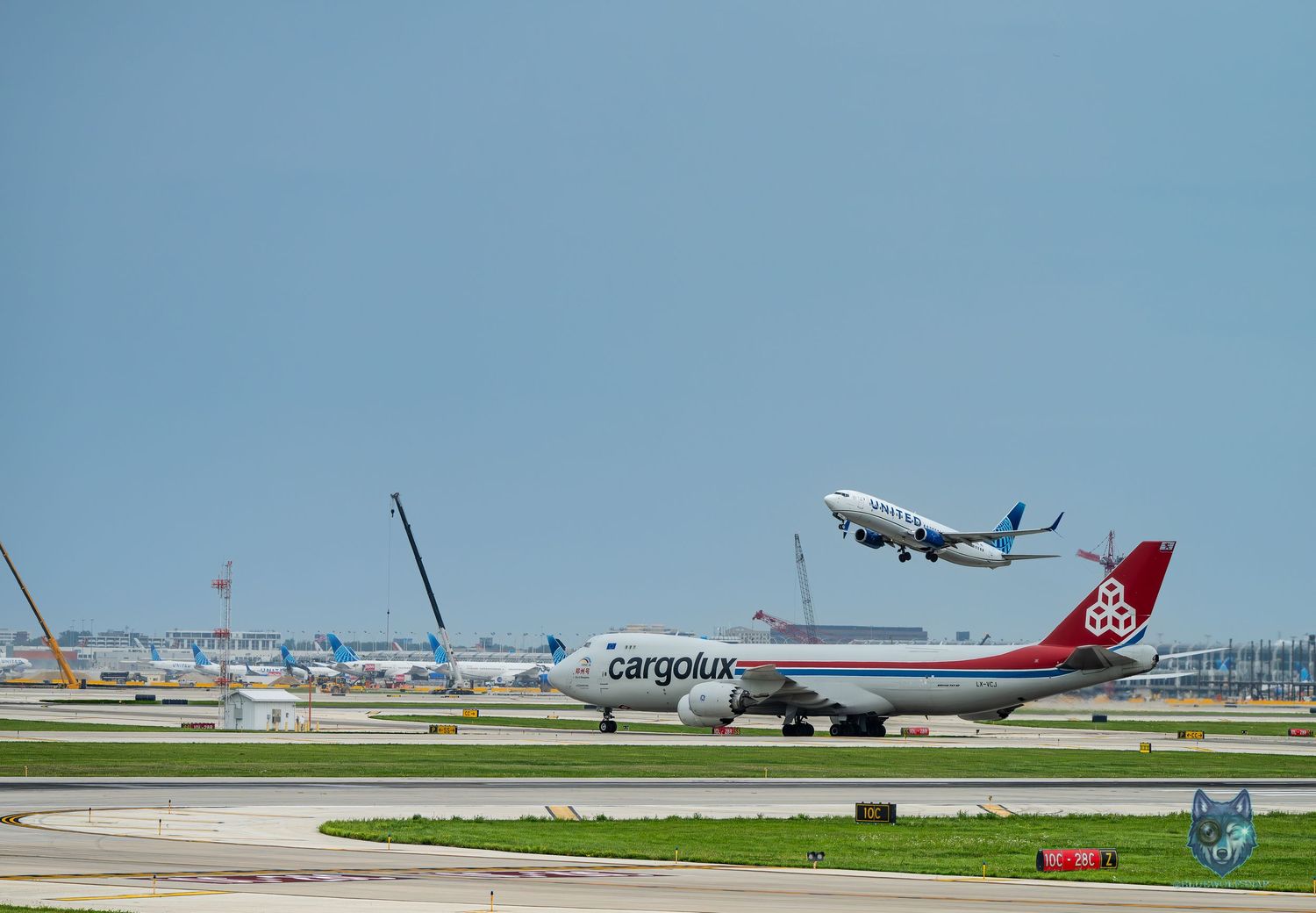 Cargolux Boeing 747 cargo plane on tarmac with another aircraft taking off at a busy international airport.