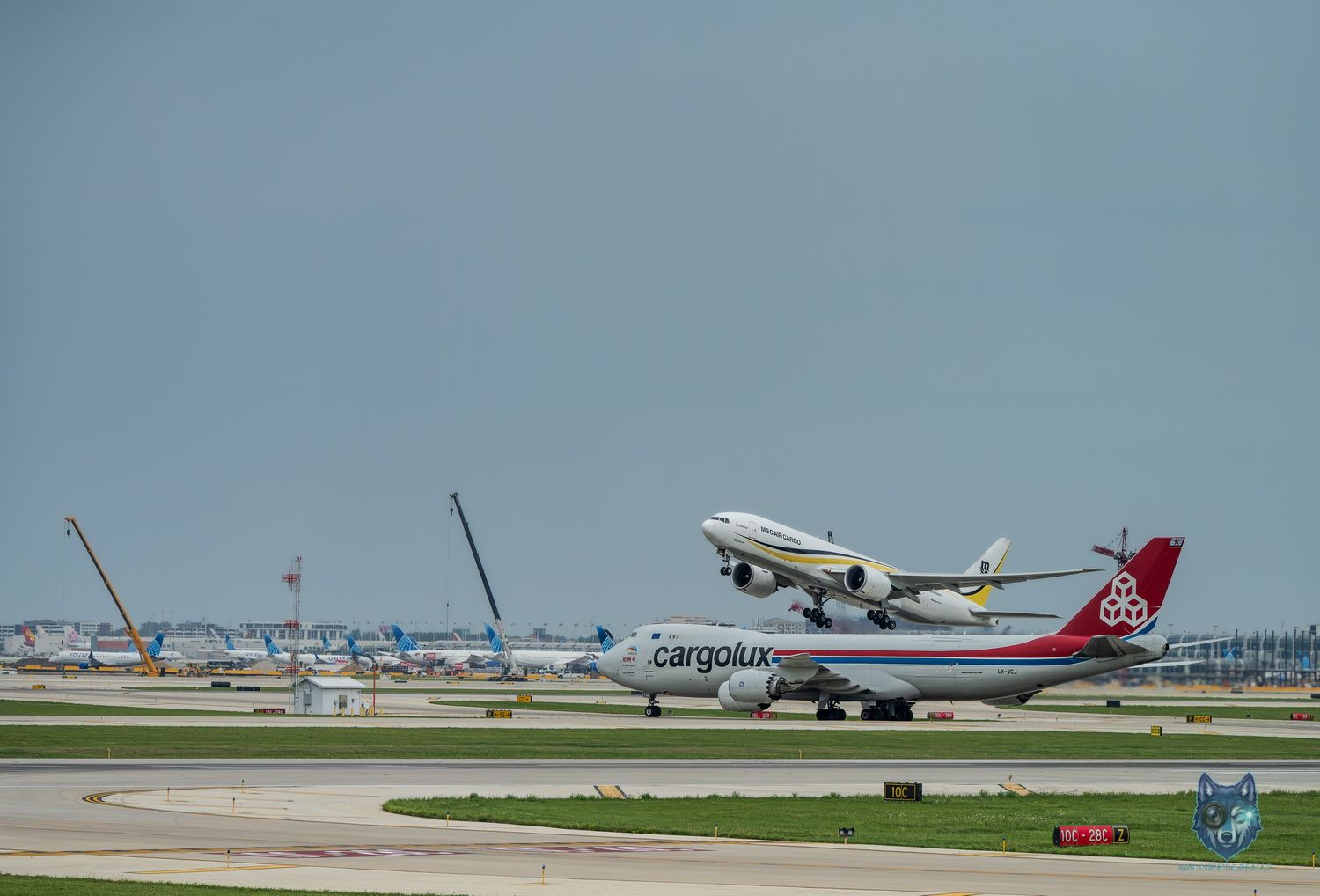Cargolux Boeing 747 cargo plane on runway with another aircraft taking off at busy international airport.