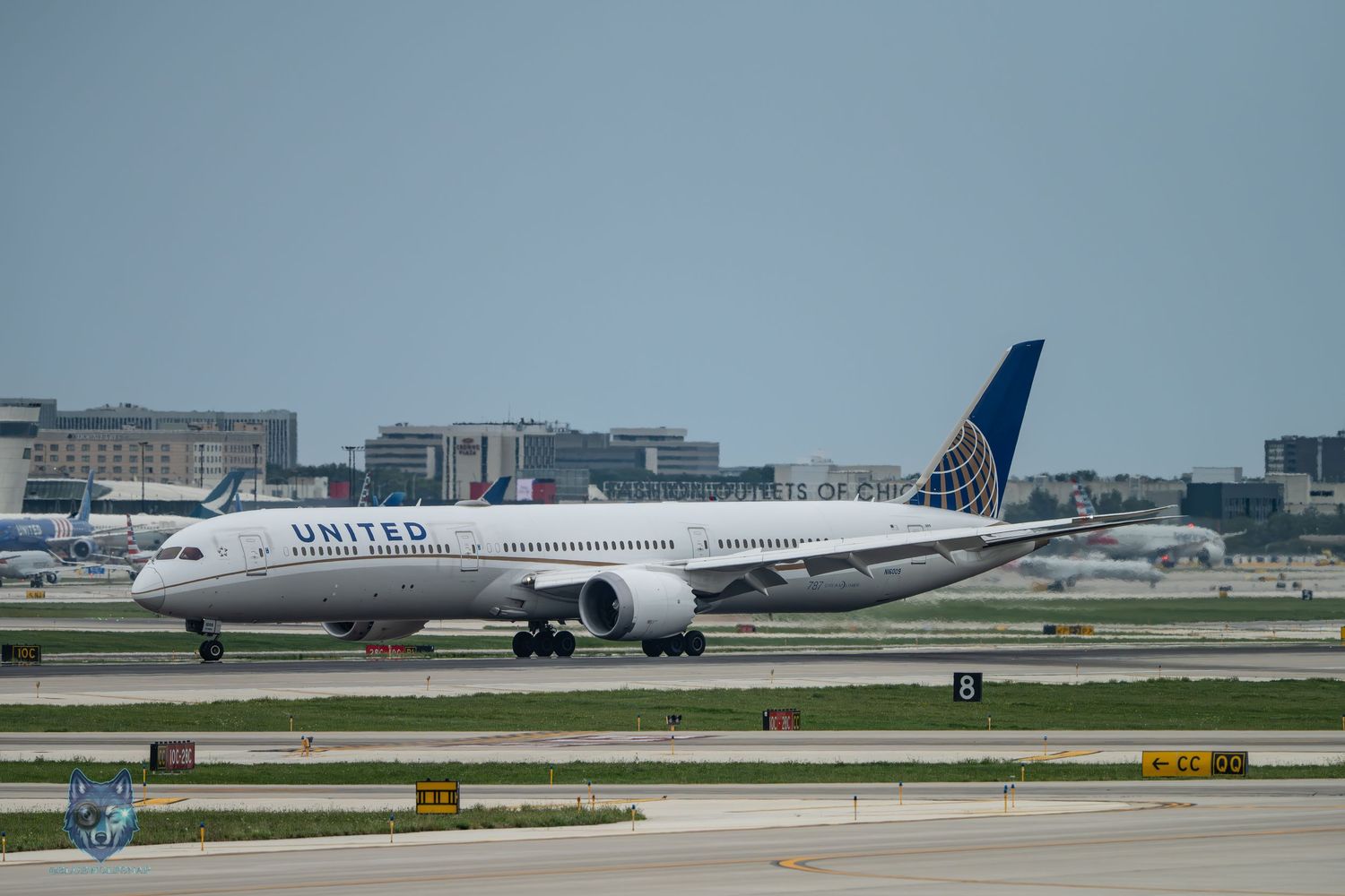United Airlines Boeing 787 Dreamliner taxiing on runway at busy international airport under overcast skies.