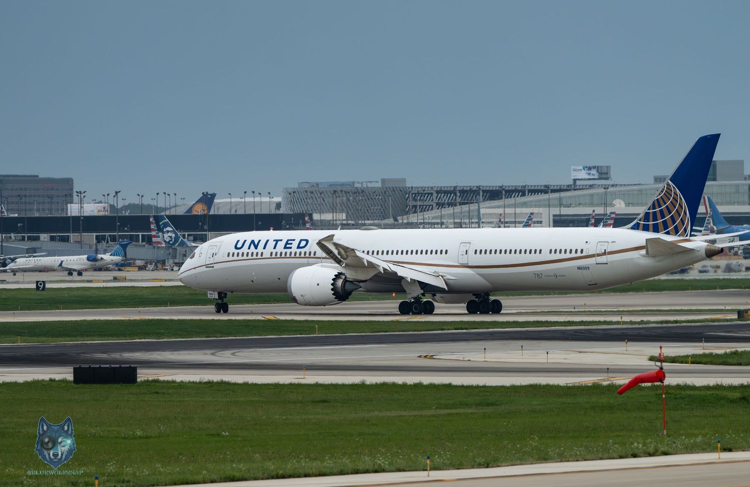 United Airlines Boeing 787 Dreamliner taxiing on runway at busy international airport on a cloudy day.