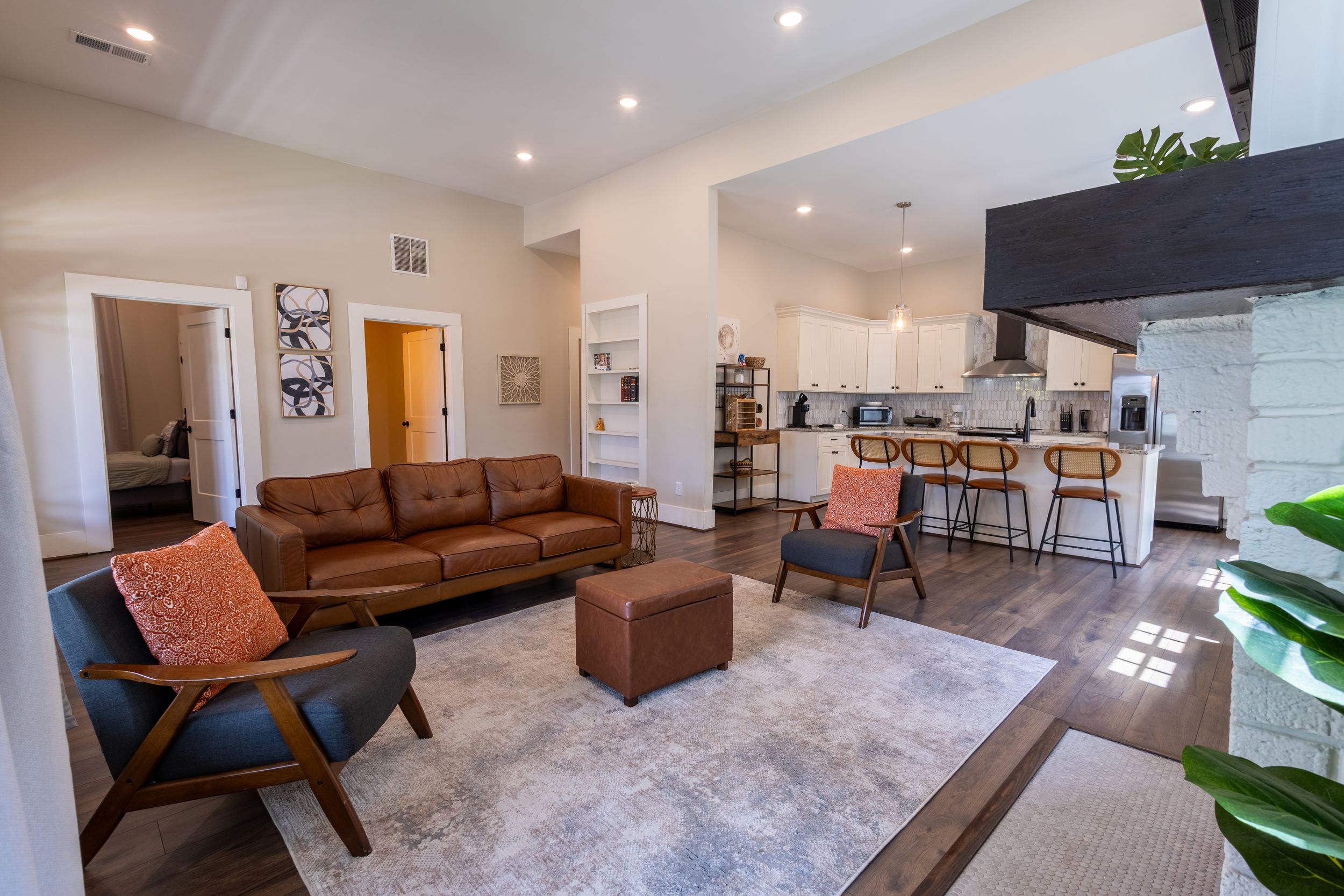 Modern open-concept living room with leather sofa, wood floors, and kitchen bar seating in a bright, contemporary home.