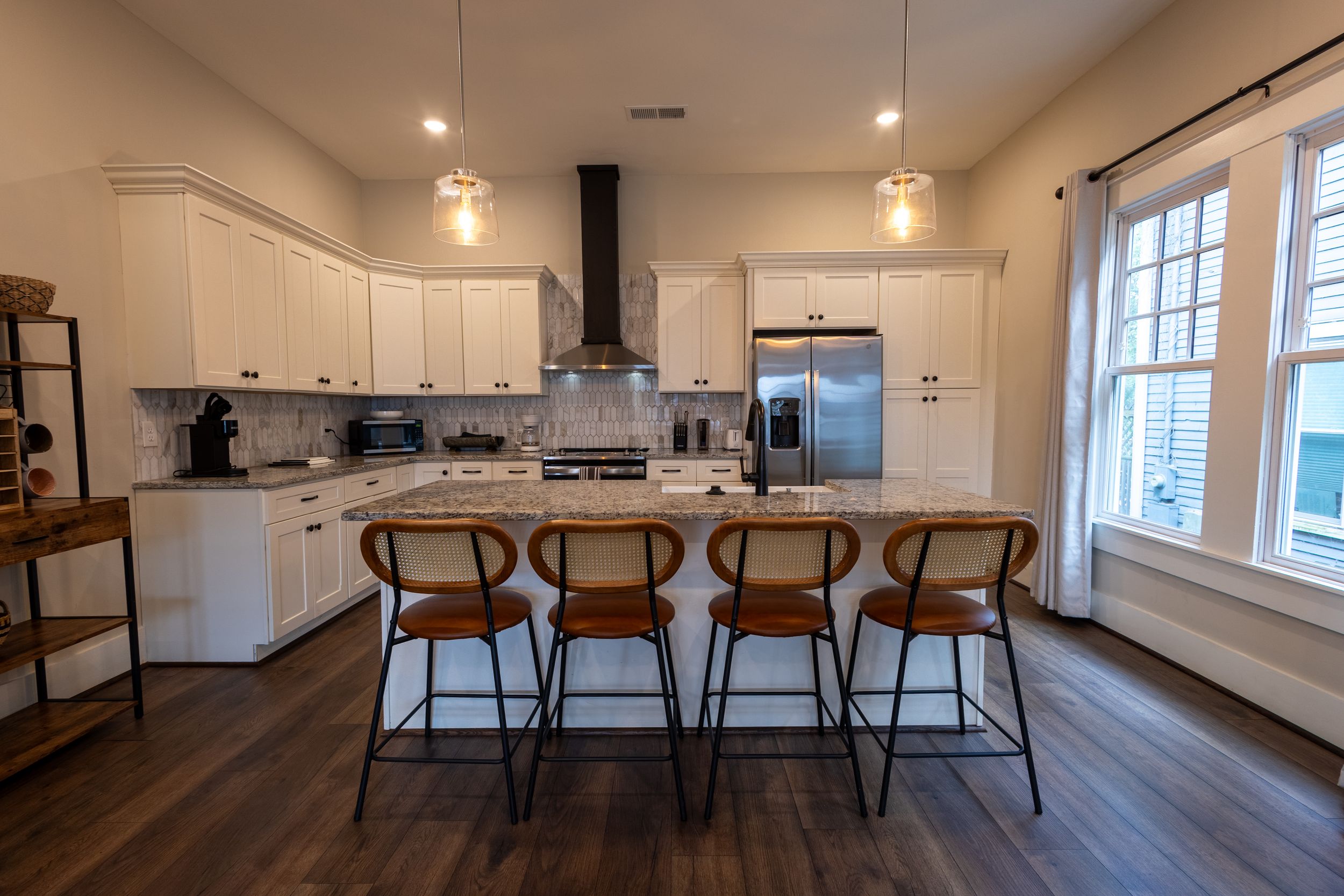Modern kitchen with white cabinets, island with brown bar stools, stainless steel appliances, and dark hardwood floors.