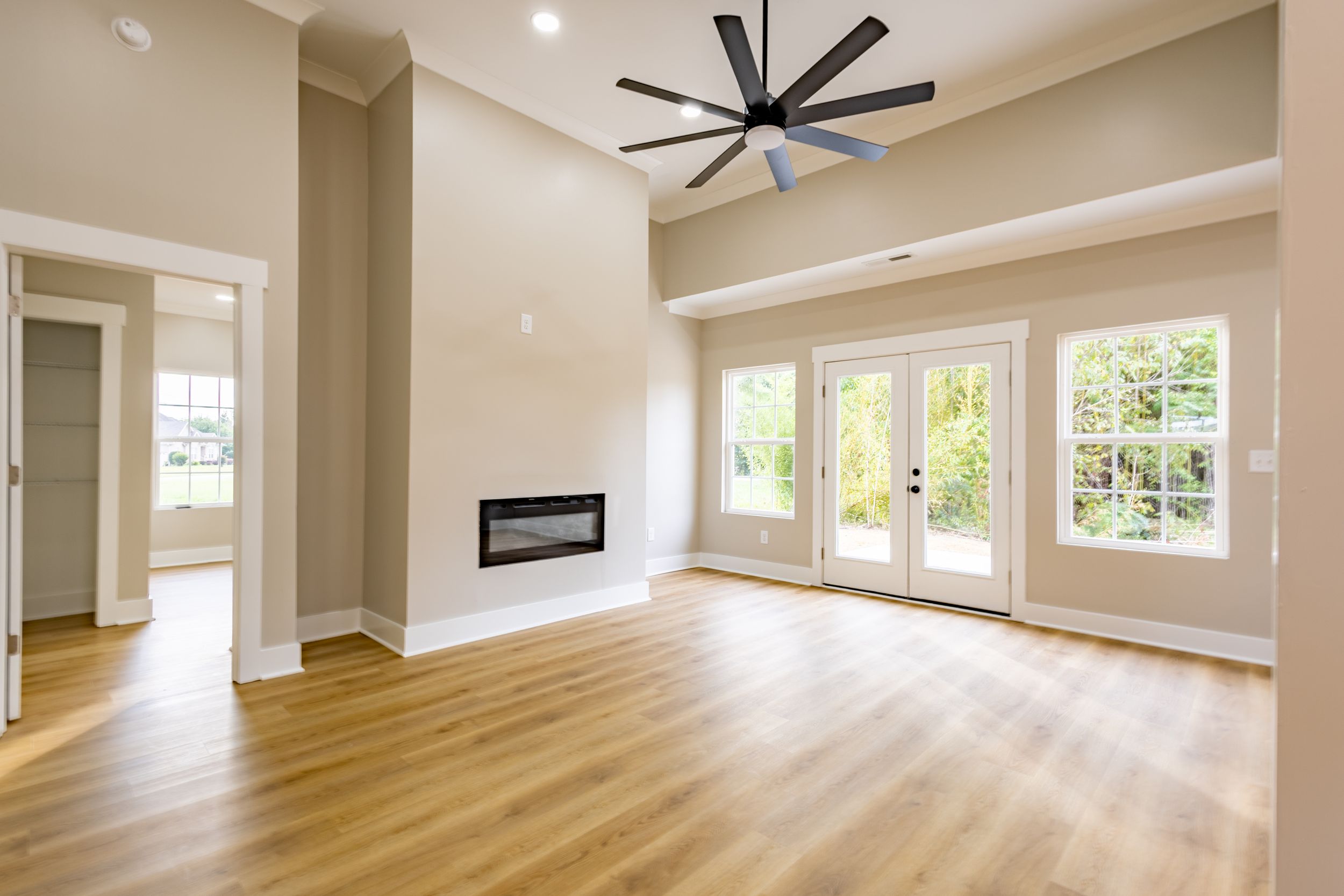 Bright open living room with hardwood floors, modern fireplace, French doors, and ceiling fan.