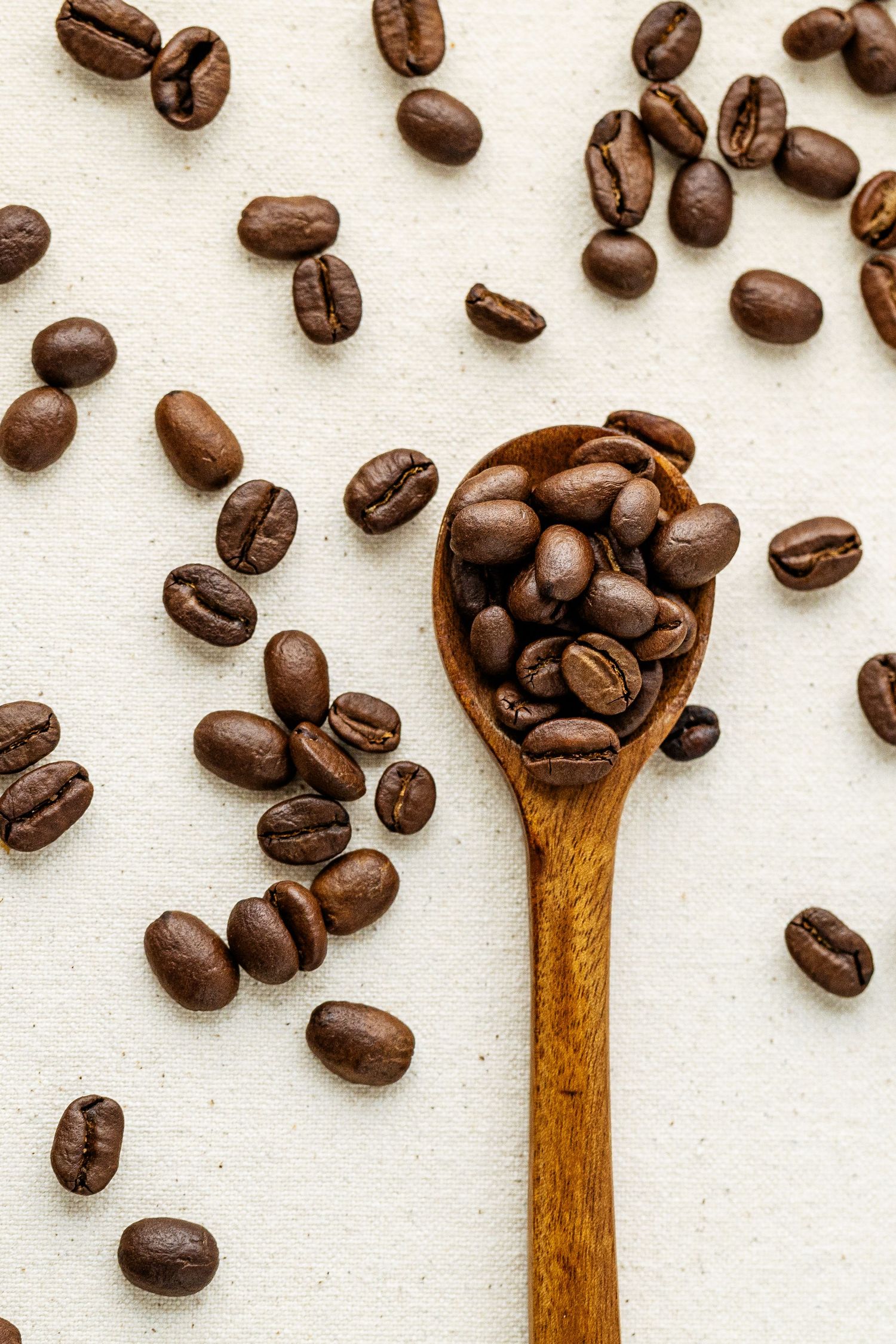 Stock photo of a wooden spoon filled with coffee beans that are scattered on a burlap surface.