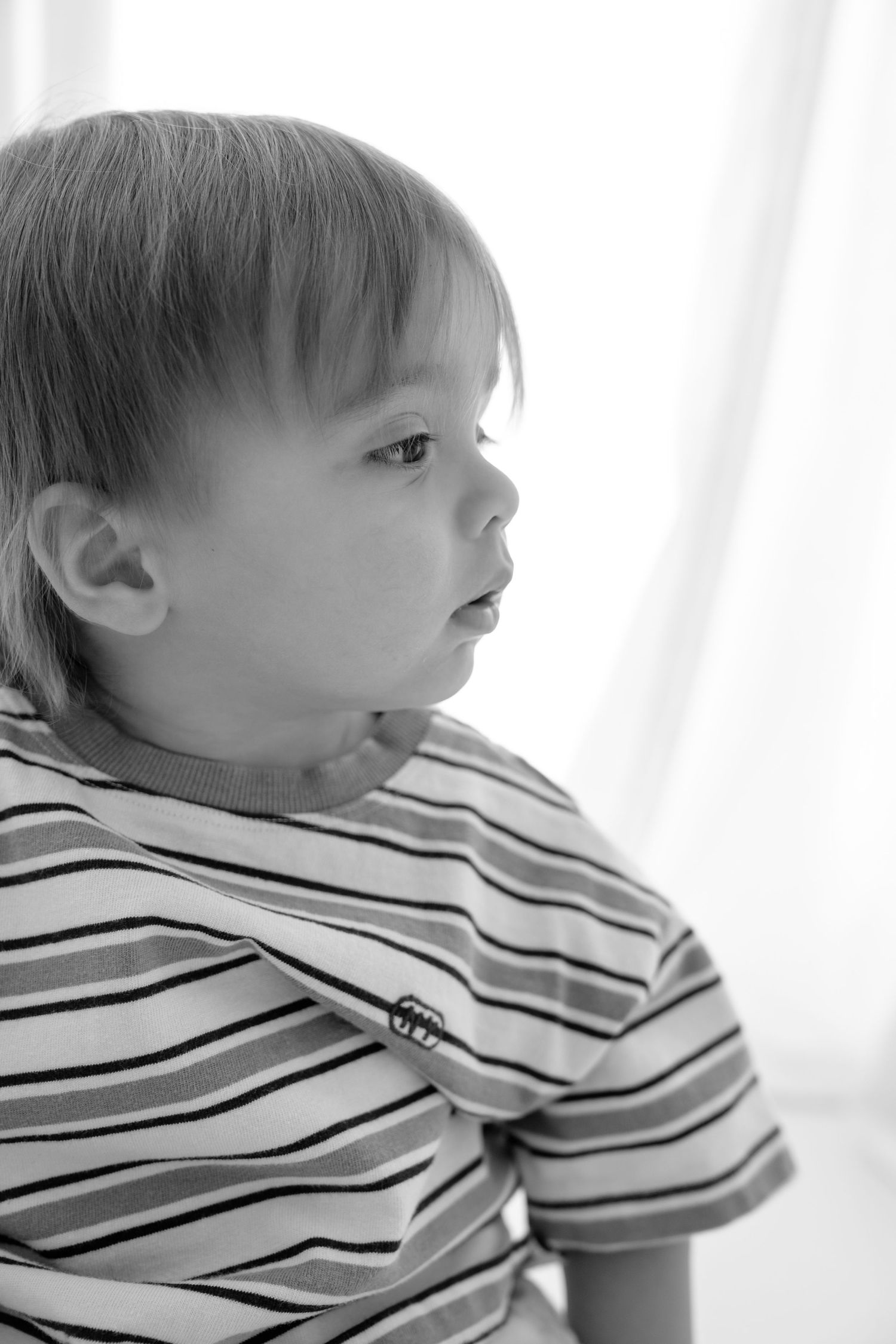 Black and white portrait of a young toddler boy in a striped t-shirt gazing thoughtfully to the side.