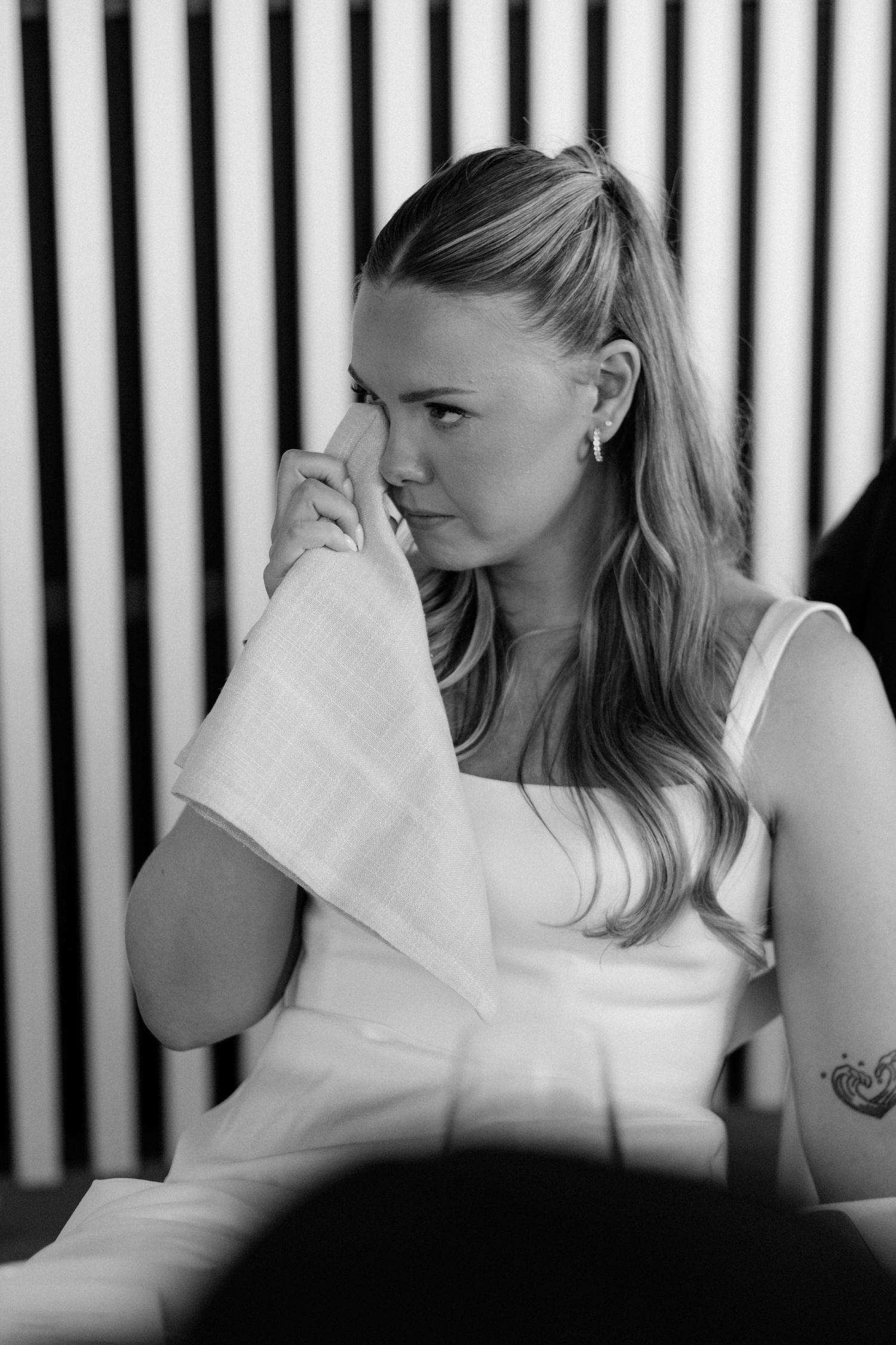A black and white portrait of an emotional bride dabbing tears with a white handkerchief during a ceremony.