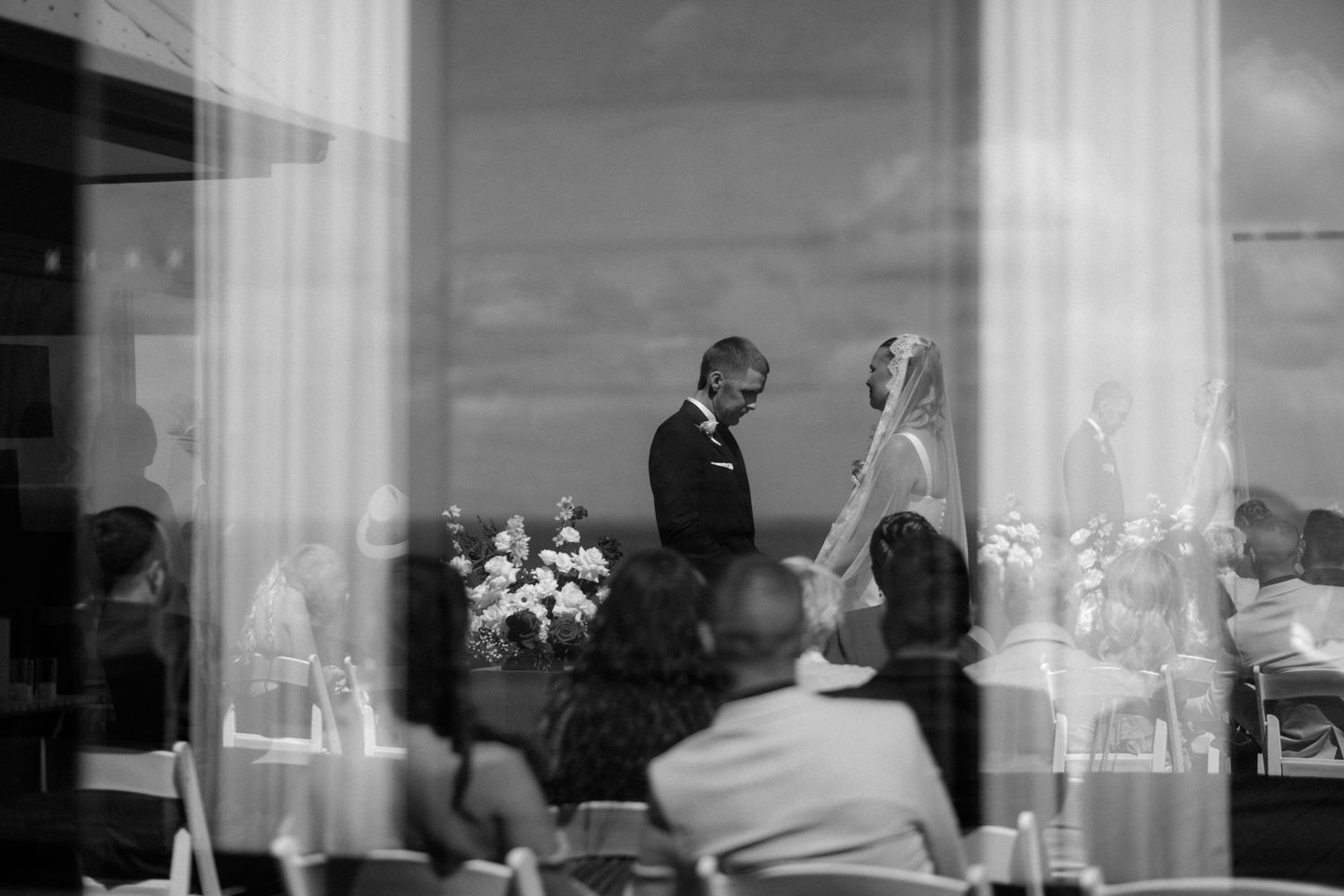 A bride and groom are reflected in glass windows during their wedding ceremony in a black and white photo.