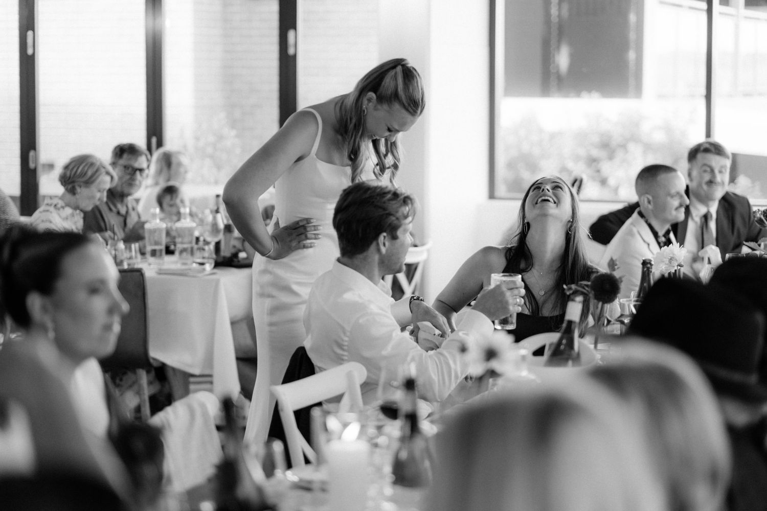 Black and white candid of guests laughing and mingling at a lively wedding reception.