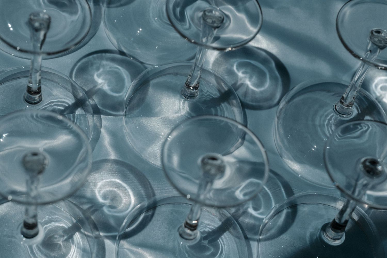Multiple crystal wine glasses submerged in clear blue water creating elegant reflections and ripples.