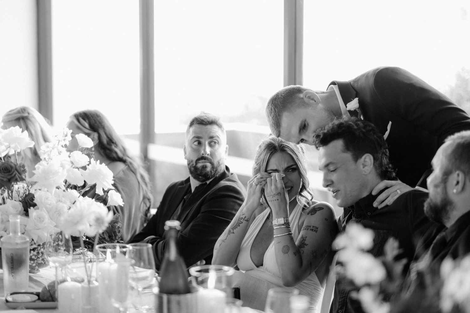 Black and white photo of wedding guests reacting emotionally during heartfelt speeches at reception.