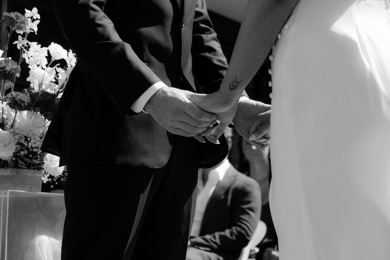 Black and white close-up of bride and groom holding hands during wedding ring exchange ceremony.