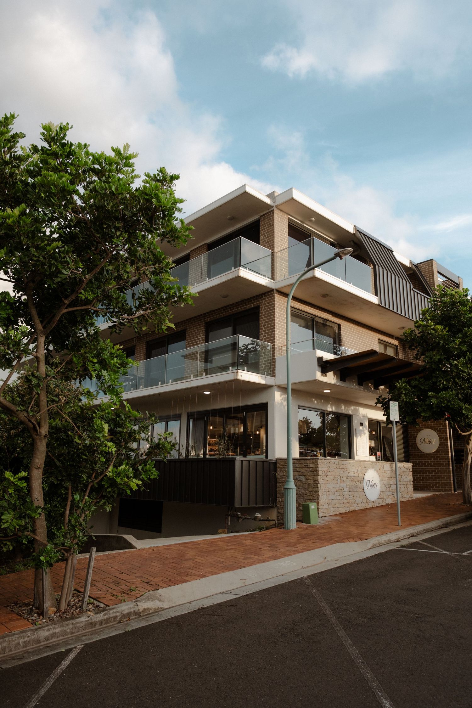 Modern multi-story wedding venue building exterior with glass balconies surrounded by lush trees.