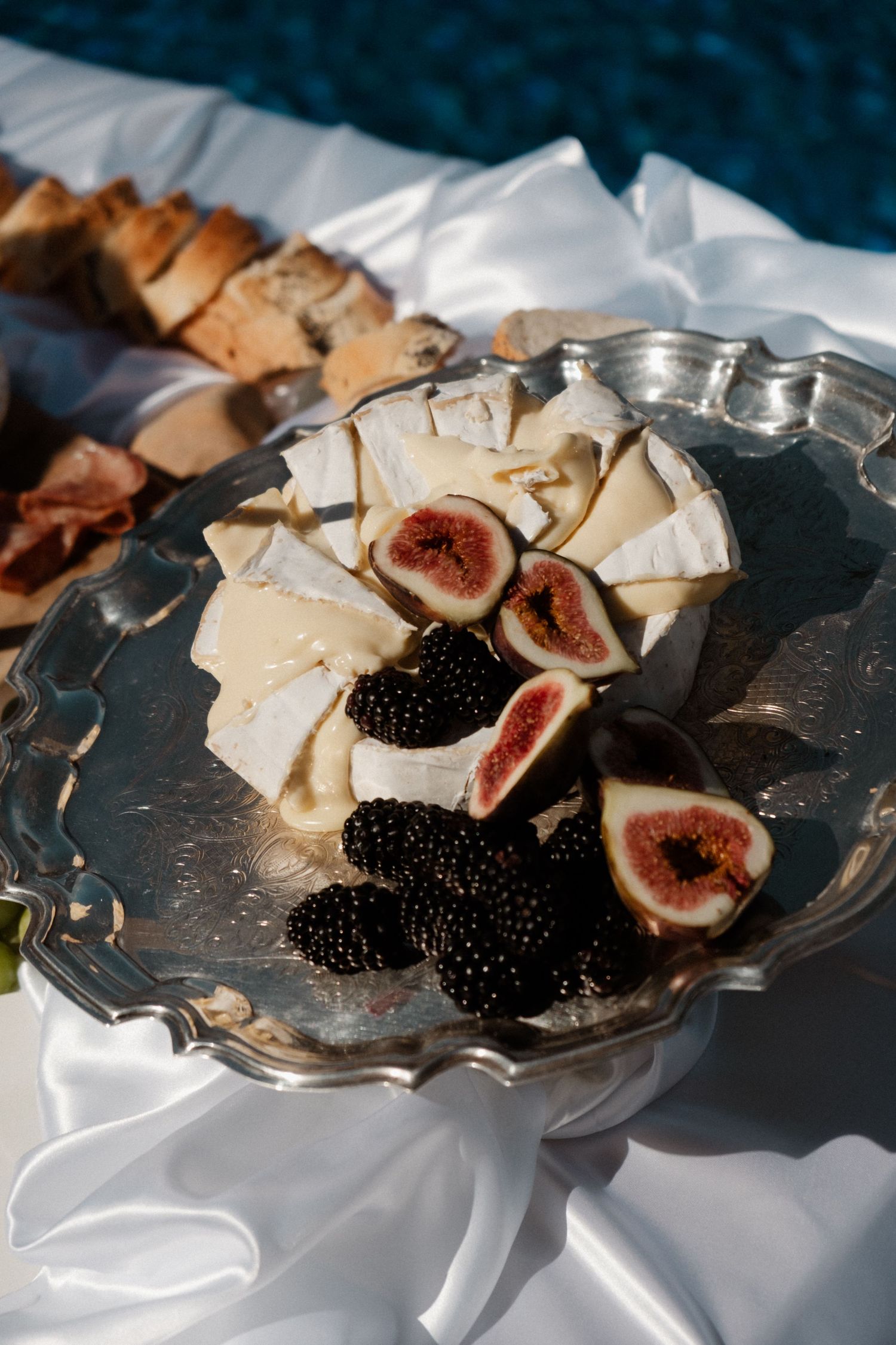 Silver platter with brie cheese, fresh figs, and blackberries served outdoors near a pool.