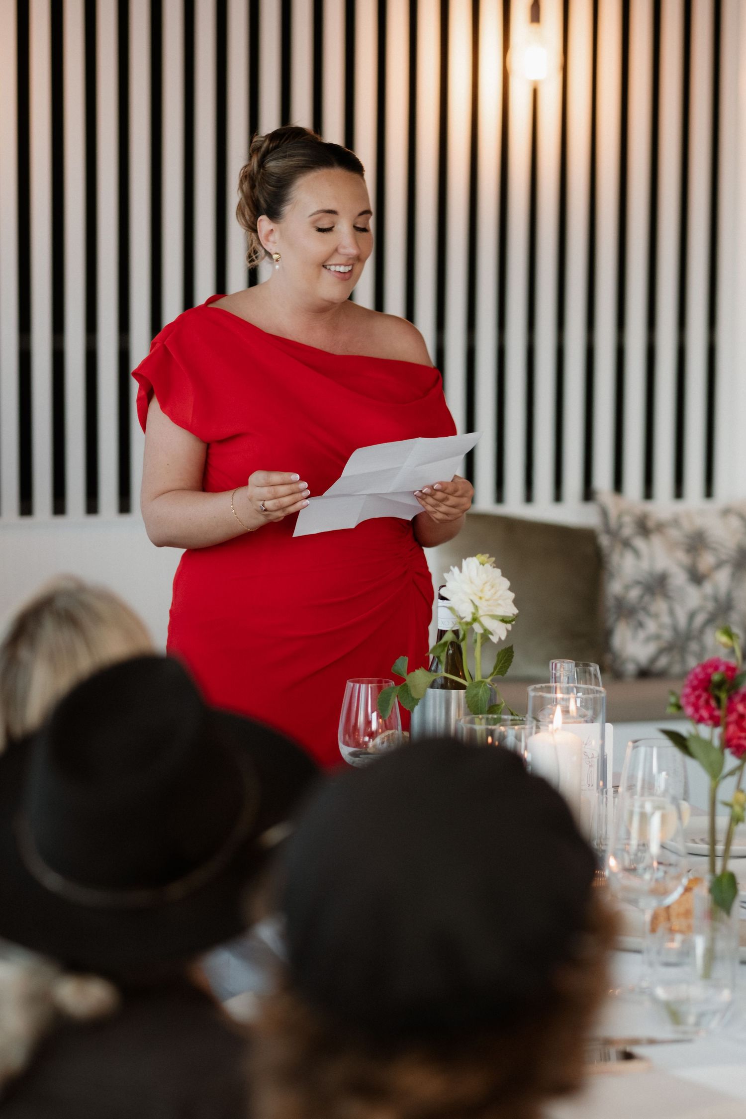 Woman in red dress giving a speech at an elegant wedding reception dinner.