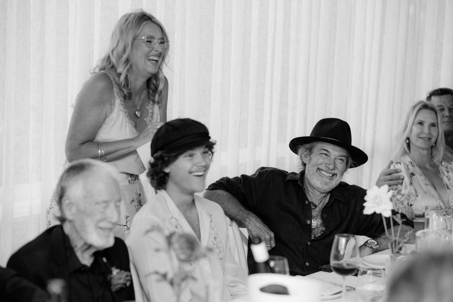 Black and white photo of a group of people laughing and enjoying a dinner party or wedding reception together.