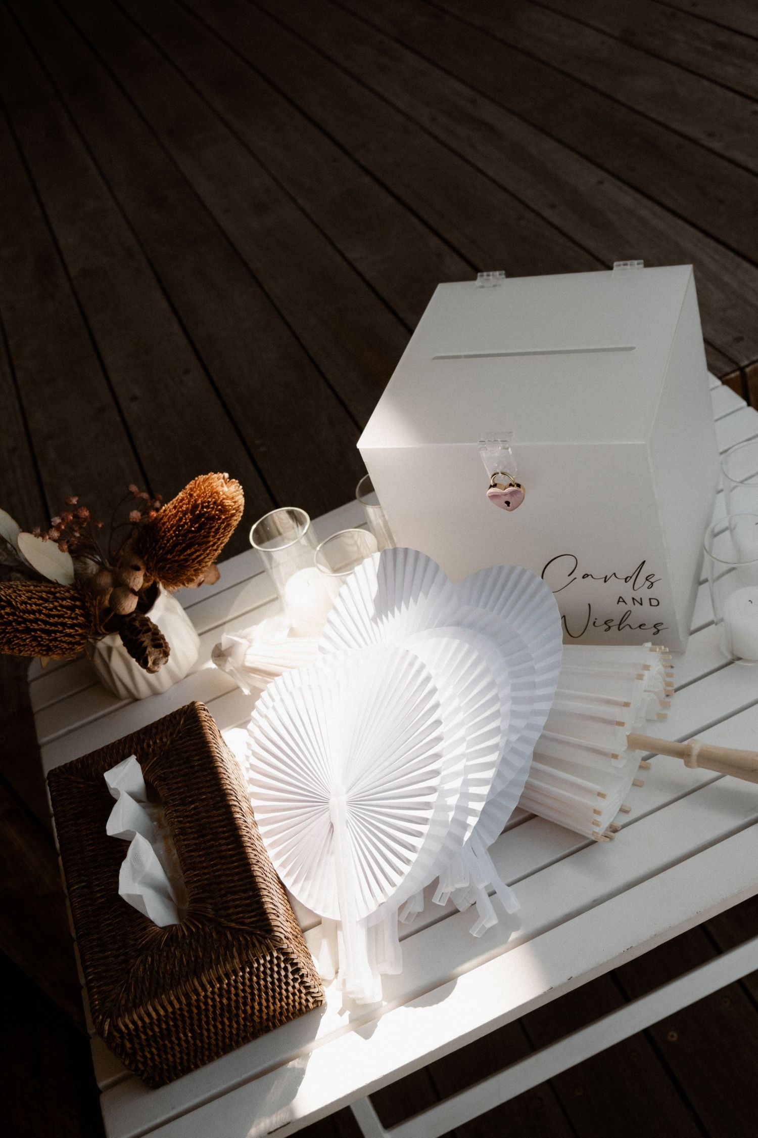 White wedding cards and wishes box with paper fans on a wooden table.