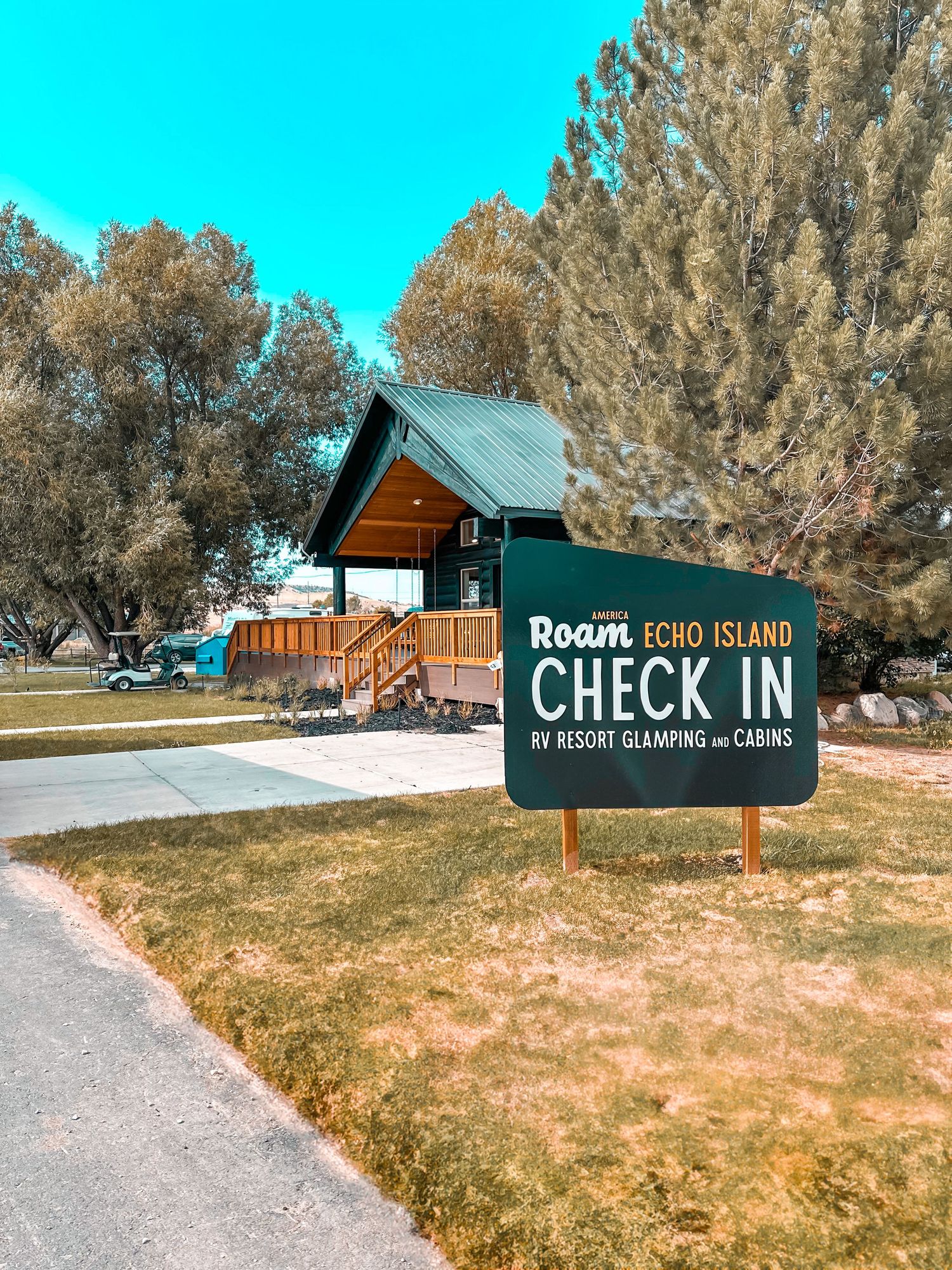 Roam Echo Island RV Resort glamping and cabins check-in sign with a wooden cabin and trees in background.