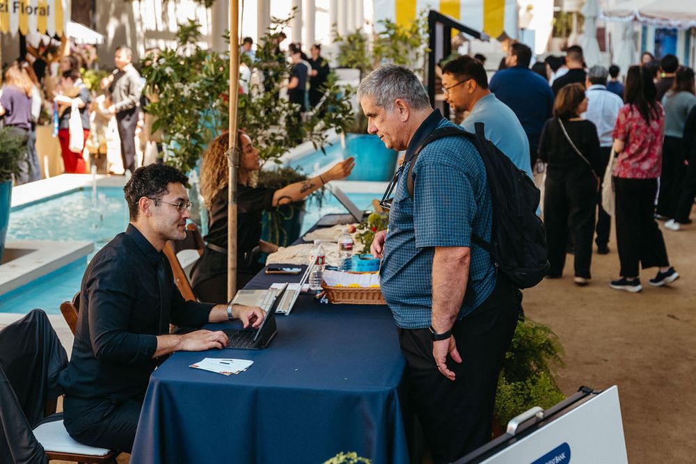 Professional registration desk at outdoor conference event with attendees networking near poolside venue.