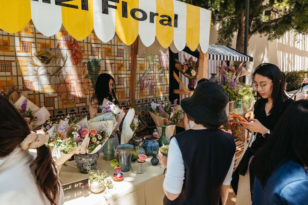 Customers browsing colorful floral arrangements at 121 Floral outdoor market booth with tiled backdrop.