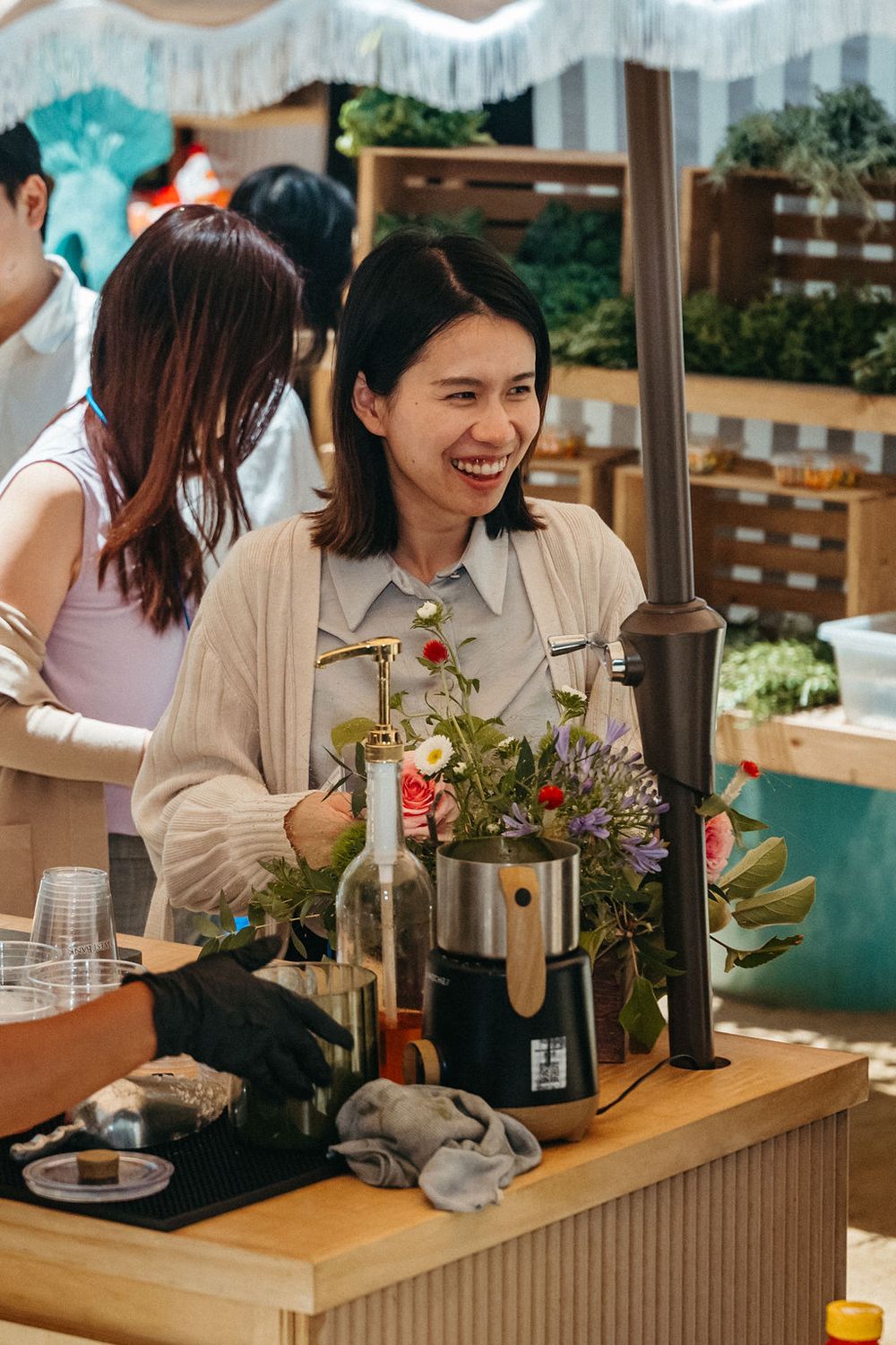 Smiling Asian woman arranging fresh flowers at an outdoor market stall with colorful blooms.