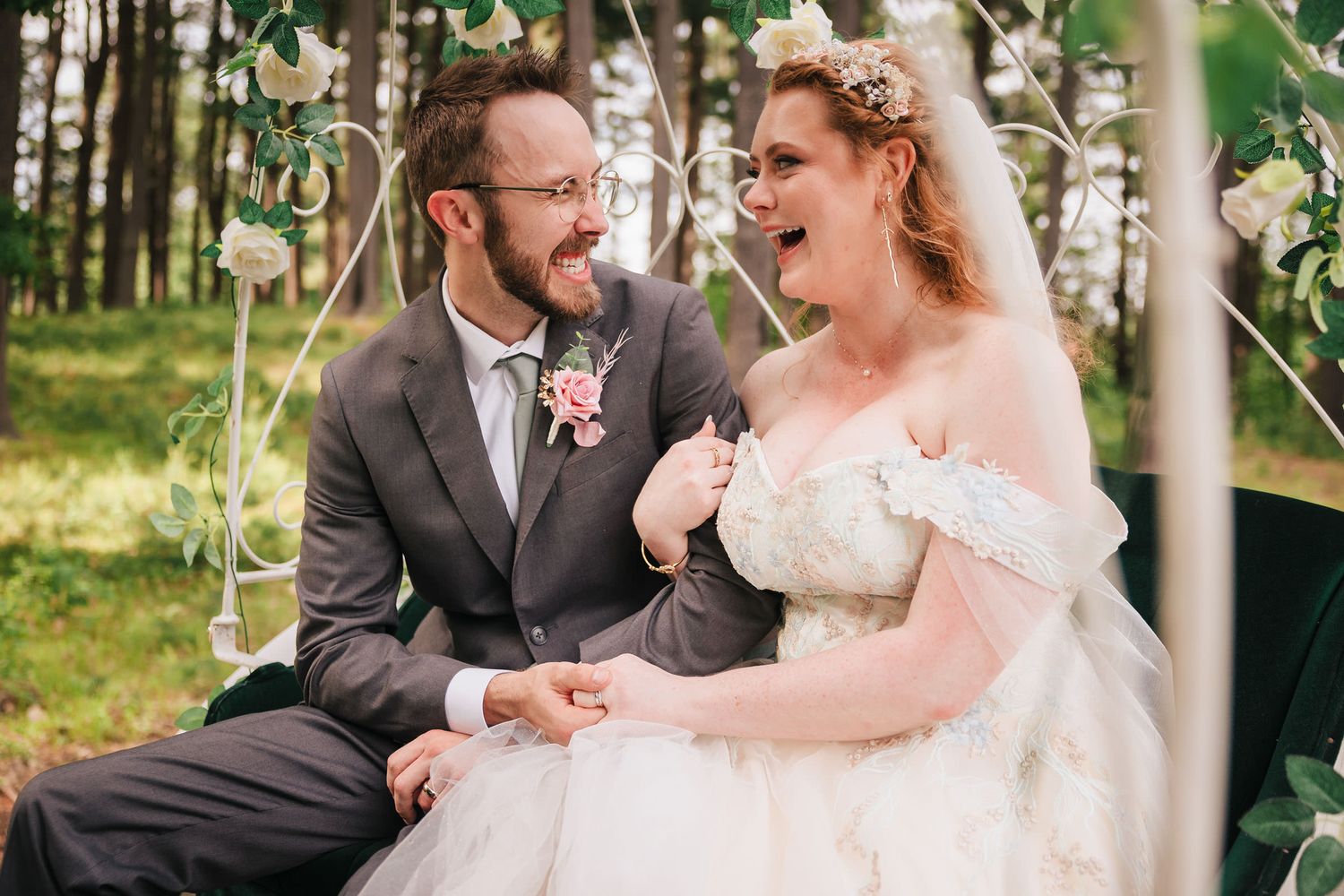 Bride and groom laughing together inside a white horse-drawn carriage decorated with roses.