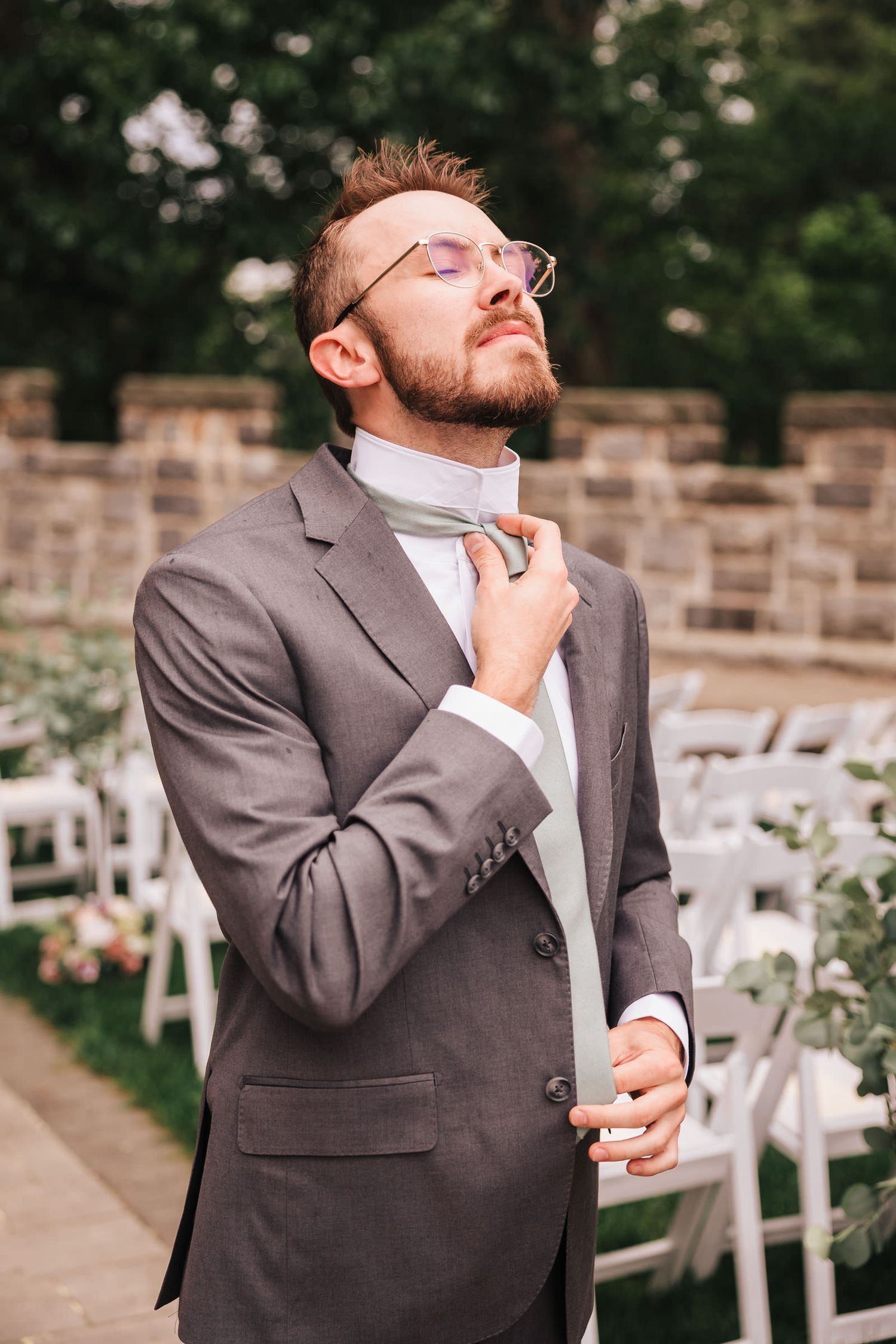 Groom laughing with his eyes closed while adjusting his tie before the ceremony at Searles Castle.