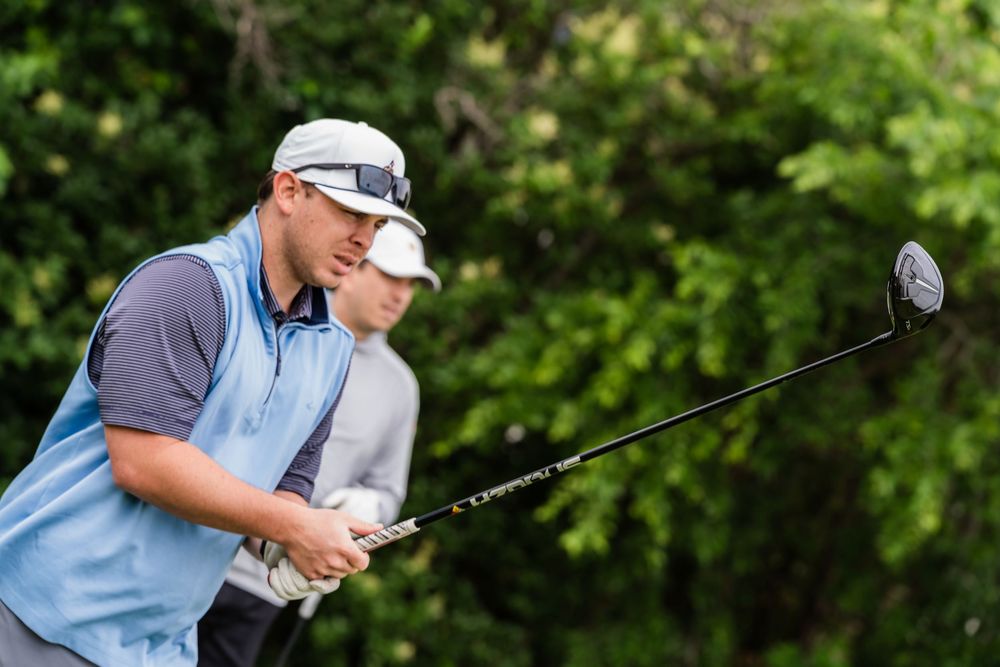 Golfer in a light blue shirt and cap preparing to swing a driver on a golf course.