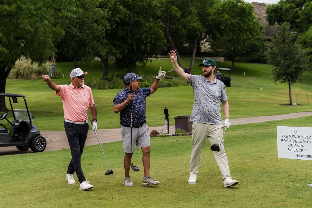 Three golfers celebrating with raised hands near a golf cart on a sunny course.