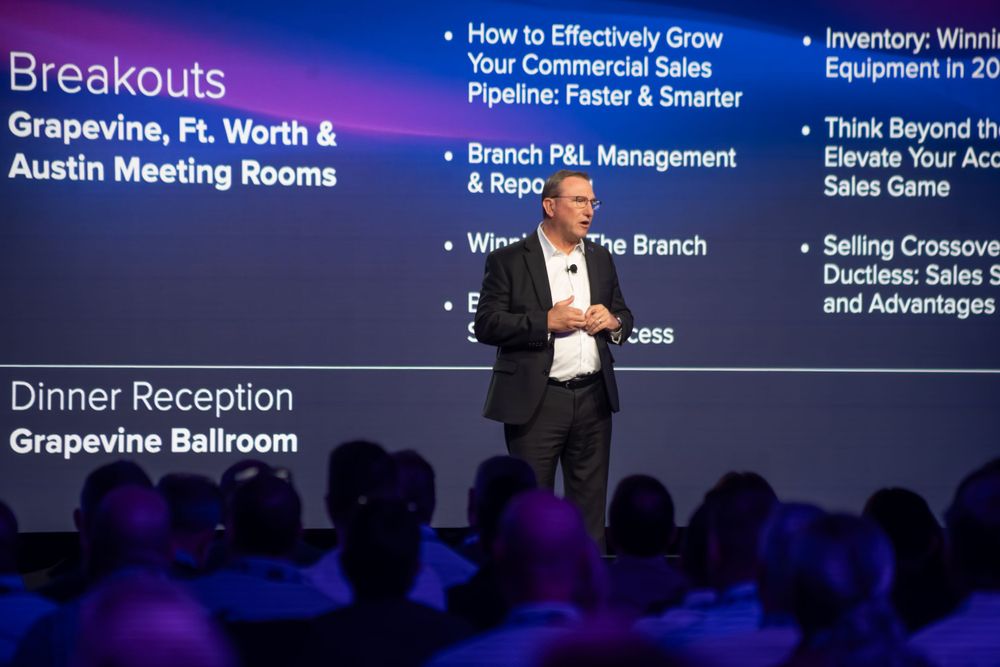 Business speaker presenting on stage with slides about sales pipeline strategies and breakout sessions.