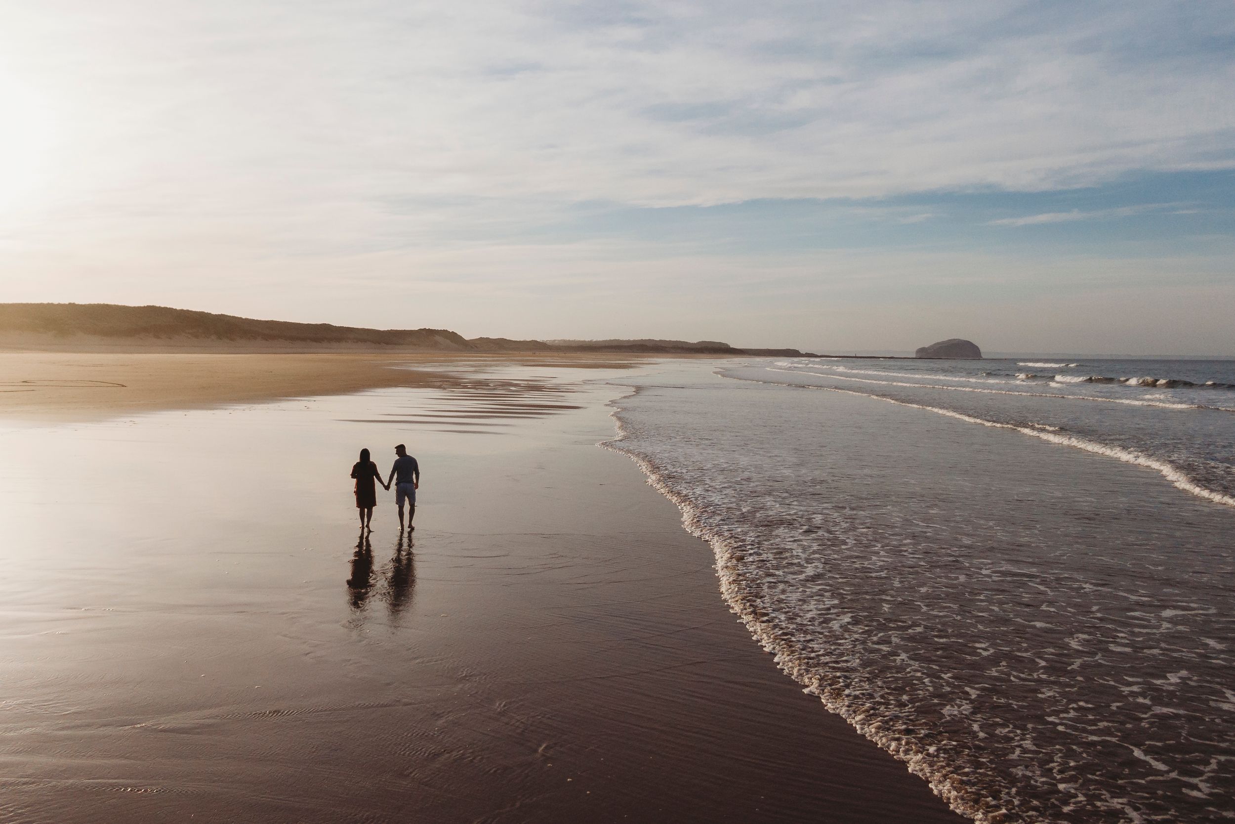 A silhouette of two people walking along a beach at sunset with waves rolling in.