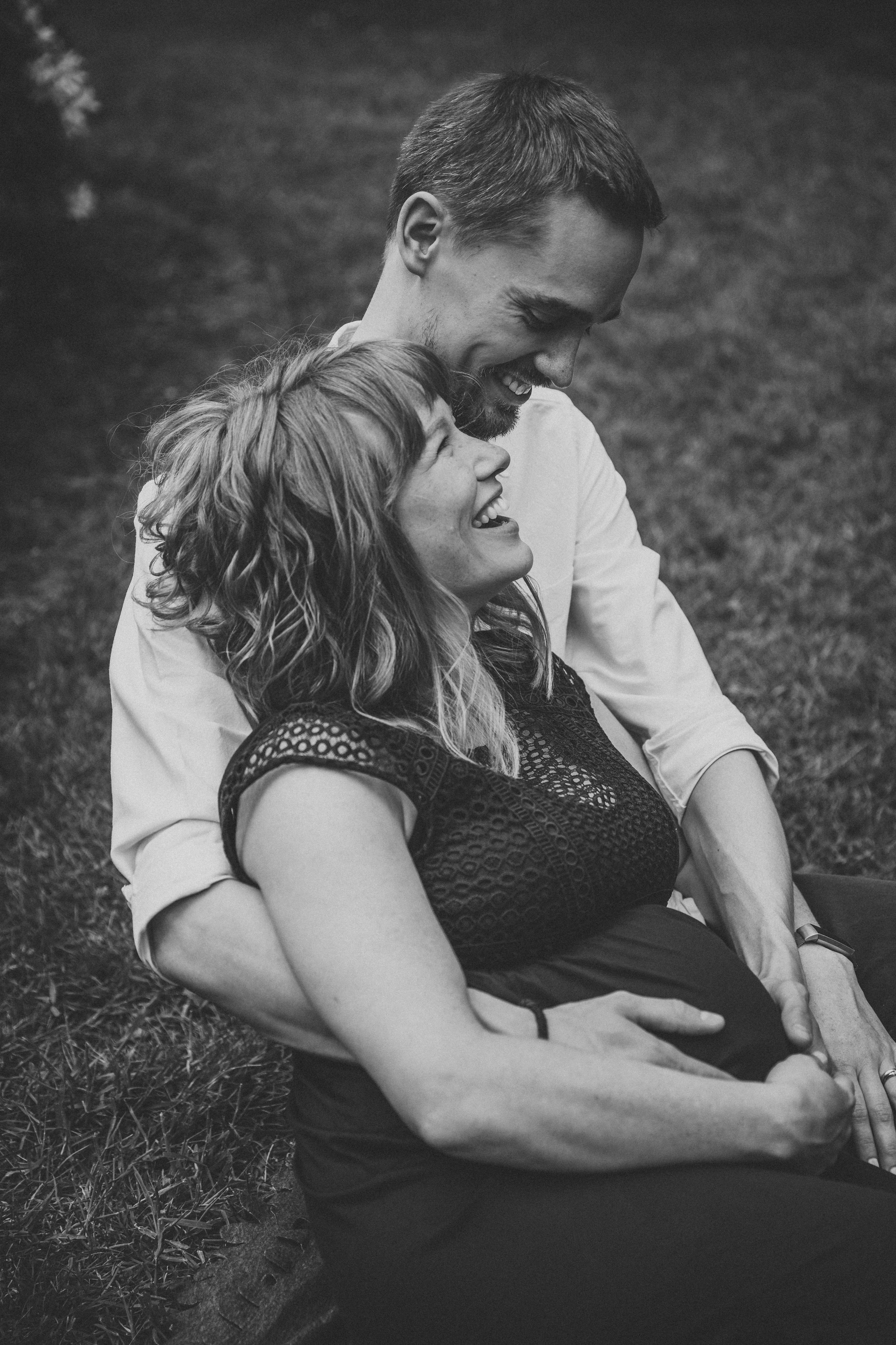 A tender black and white photograph of a couple embracing on grass.