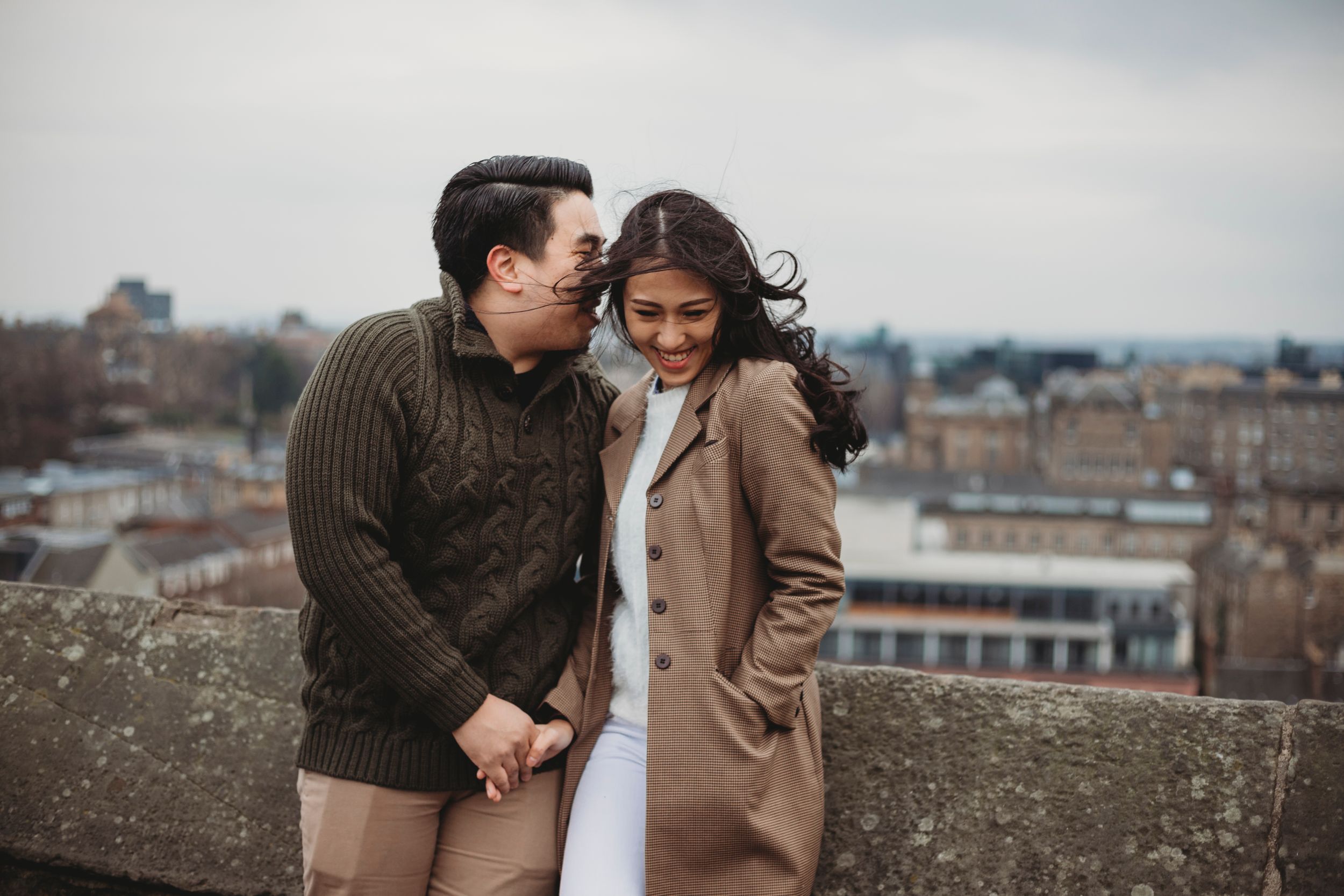 Romantic couple sharing an intimate moment on a city rooftop overlooking urban buildings on an overcast day.
