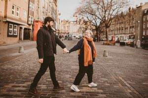 A couple holding hands while walking along cobblestone streets in autumn.