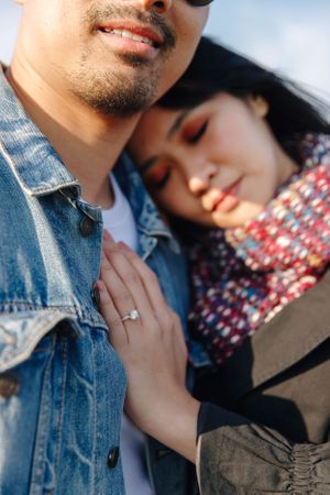 Close-up shot of couple embracing outdoors with sunlit denim jacket and patterned scarf.