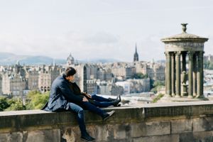 A lone figure sits overlooking the historic Edinburgh cityscape from Calton Hill.