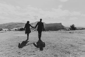 A black and white silhouette of a couple holding hands while walking across a hilltop.