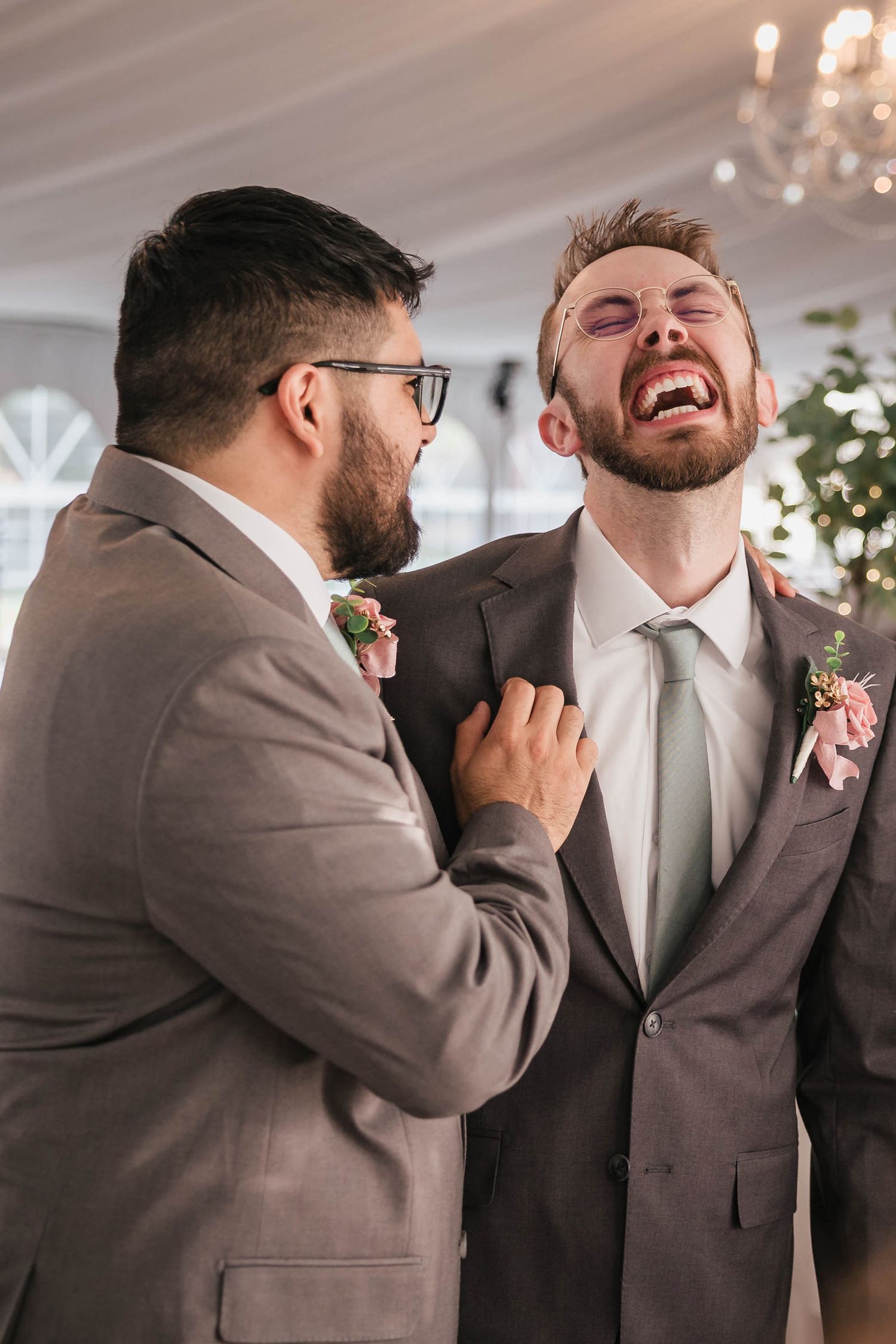 Two groomsmen laughing together, one with his head thrown back mid-laugh.