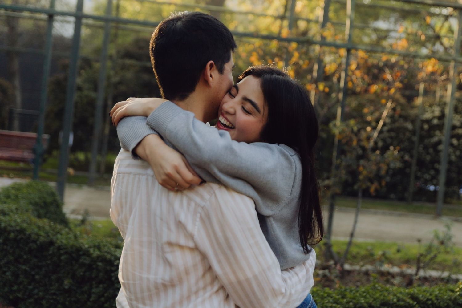 Affectionate young couple embracing in an outdoor garden setting with warm autumn sunlight in background.