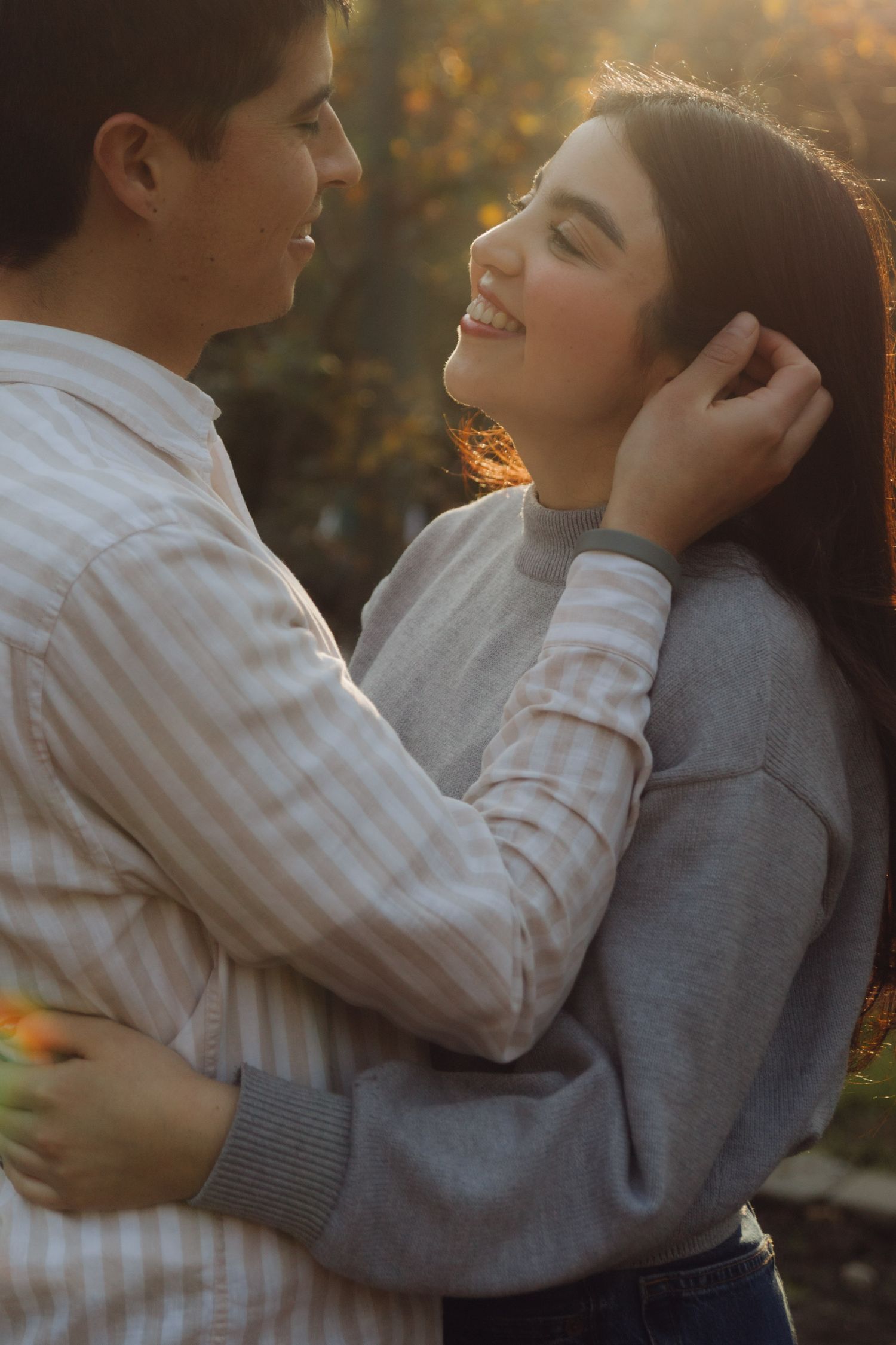 Young couple gazing at each other lovingly in warm sunset light, man gently touching womans hair.
