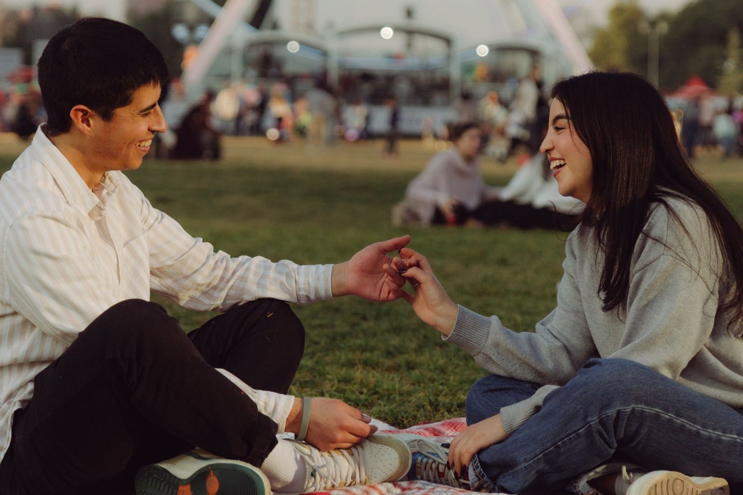 Happy young couple holding hands and laughing together at an outdoor festival on a picnic blanket.