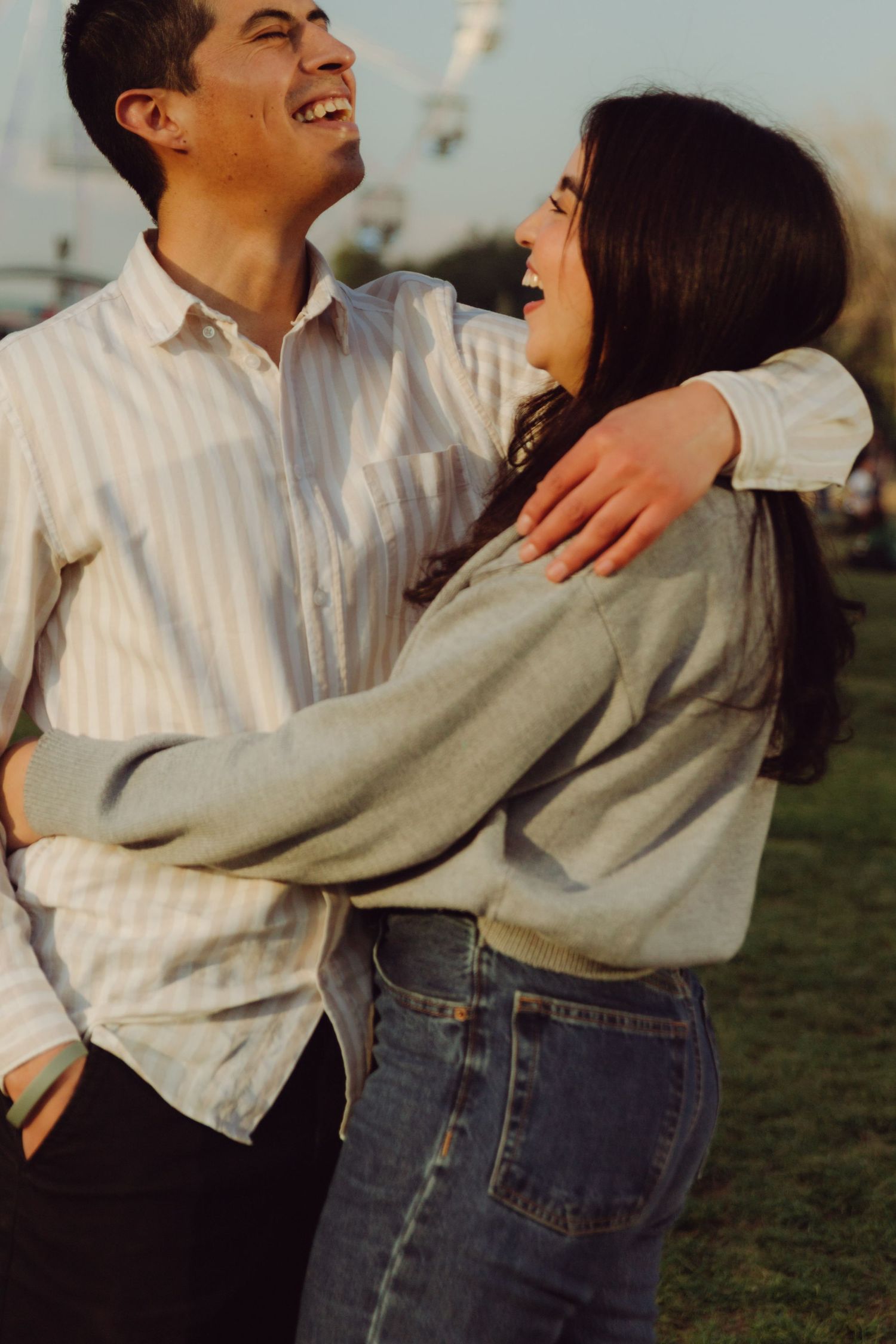 Happy young couple laughing and hugging each other at an amusement park during sunset.