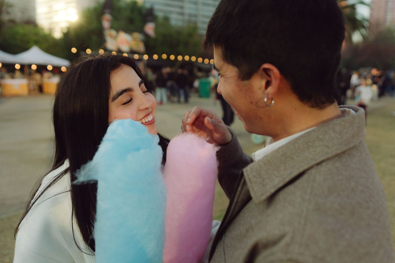 Happy couple laughing together while holding colorful cotton candy at an evening fair.