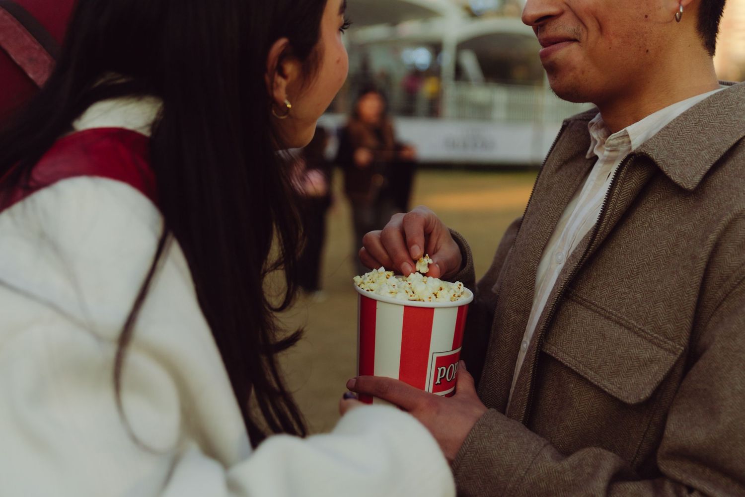 Romantic couple sharing popcorn from a striped bucket at an amusement park.