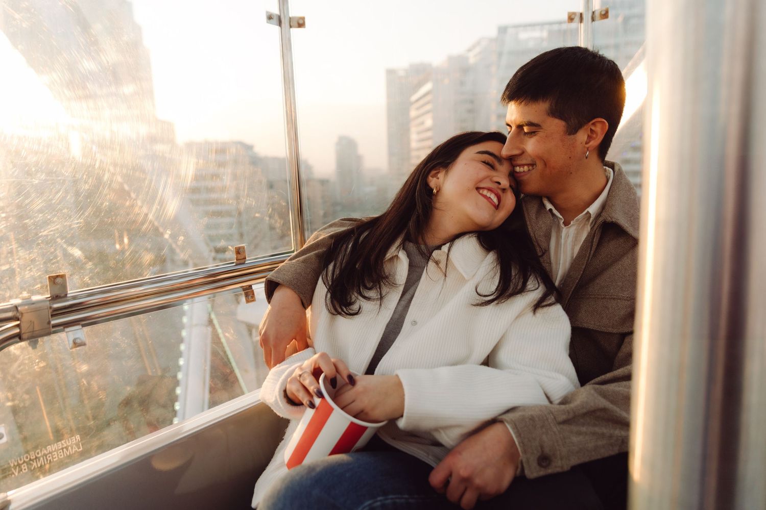 Loving couple embracing and smiling in a Ferris wheel cabin at golden hour.