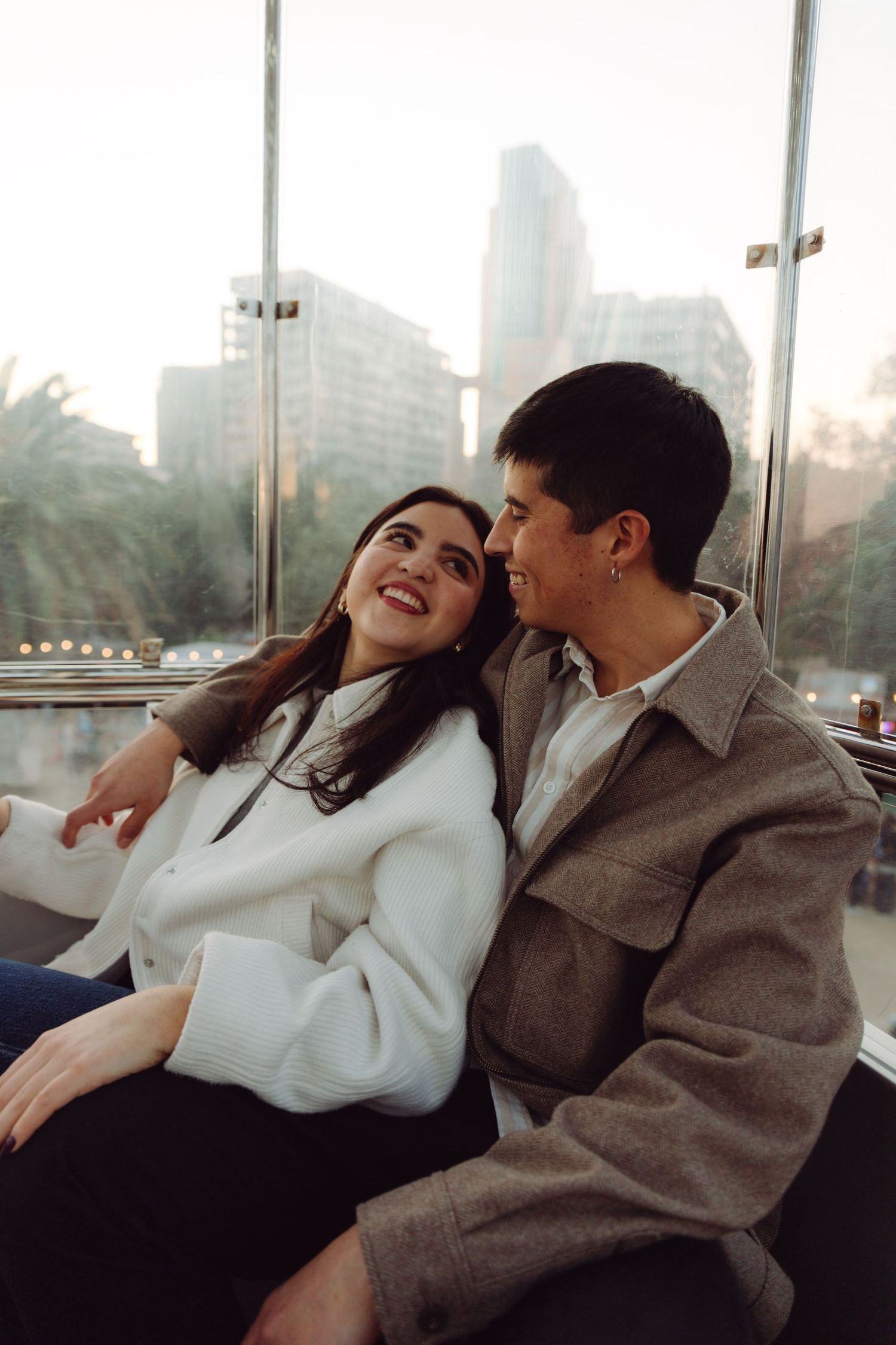 Cheerful couple sitting close together in a Ferris wheel with urban skyline backdrop.