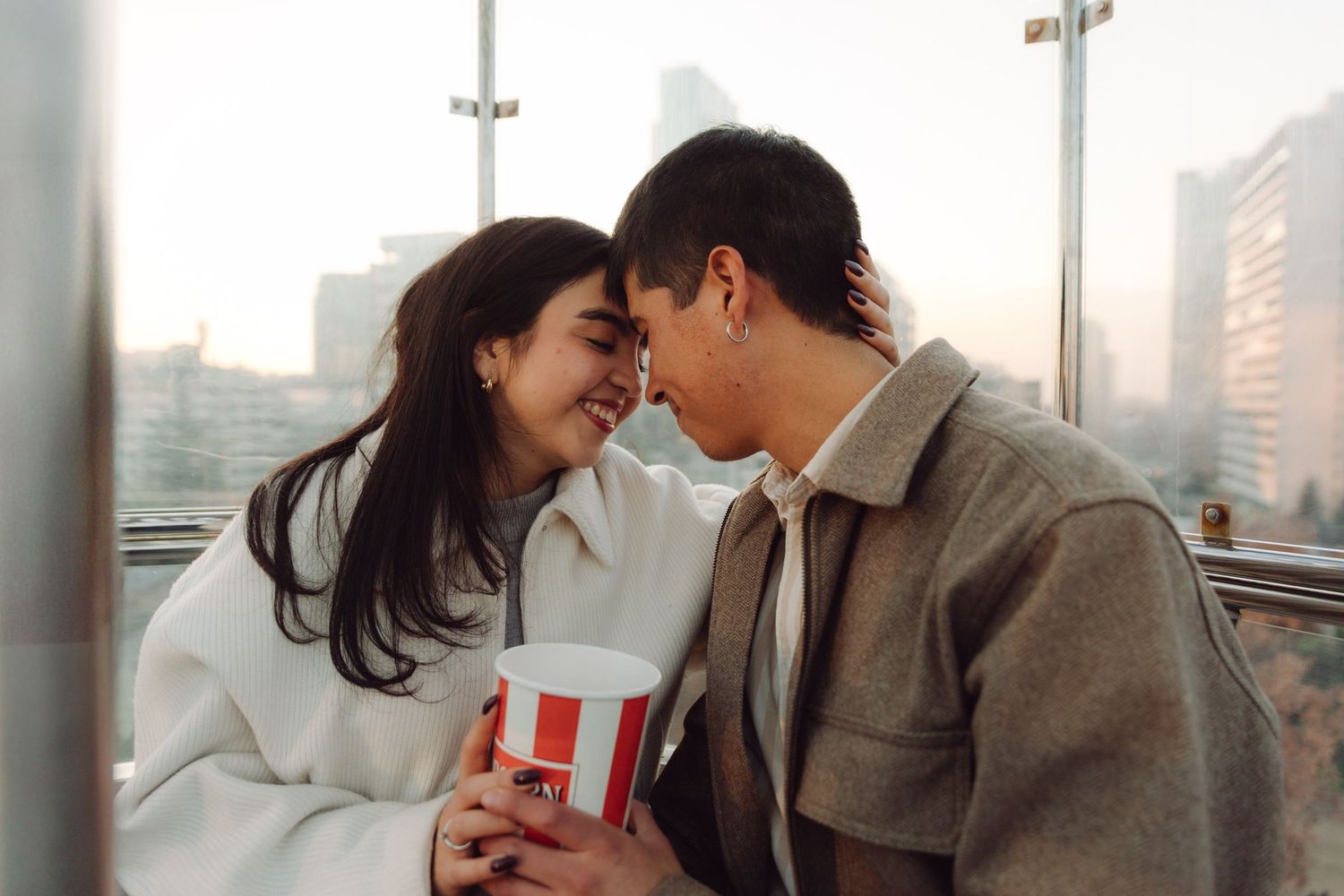 Happy couple sharing intimate moment on Ferris wheel with city skyline backdrop.