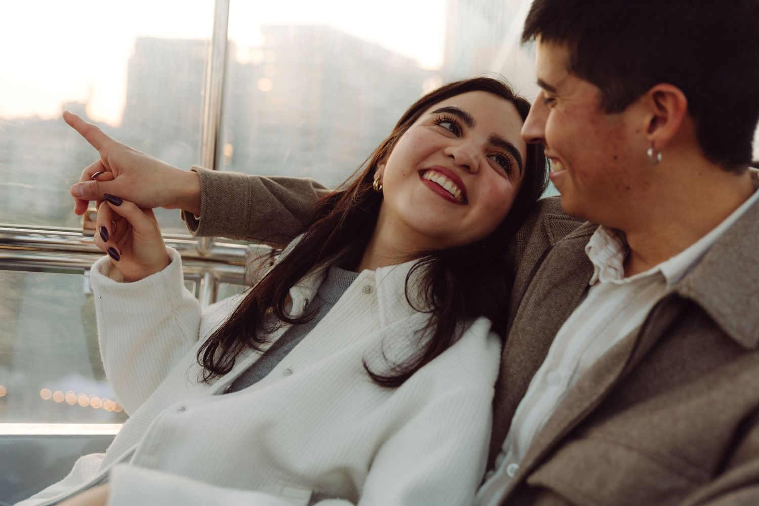 Joyful couple laughing together on Ferris wheel, woman pointing at city view.