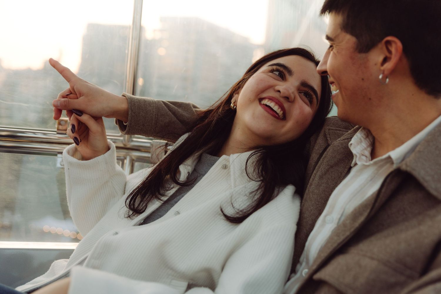 Happy couple smiling and laughing together on Ferris wheel with city backdrop.