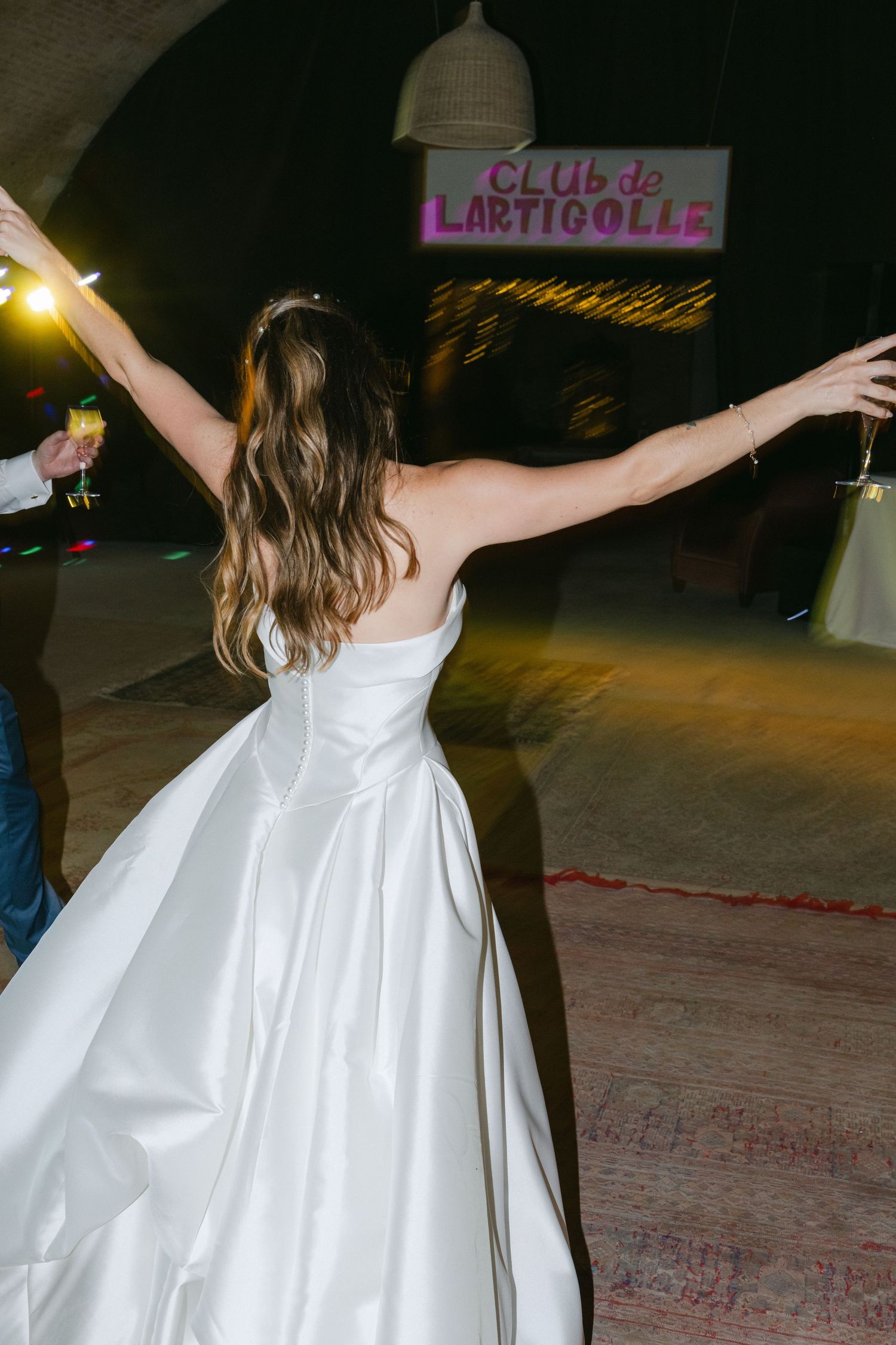 Bride in white gown dancing with arms outstretched at Club de Lartigolle wedding reception.