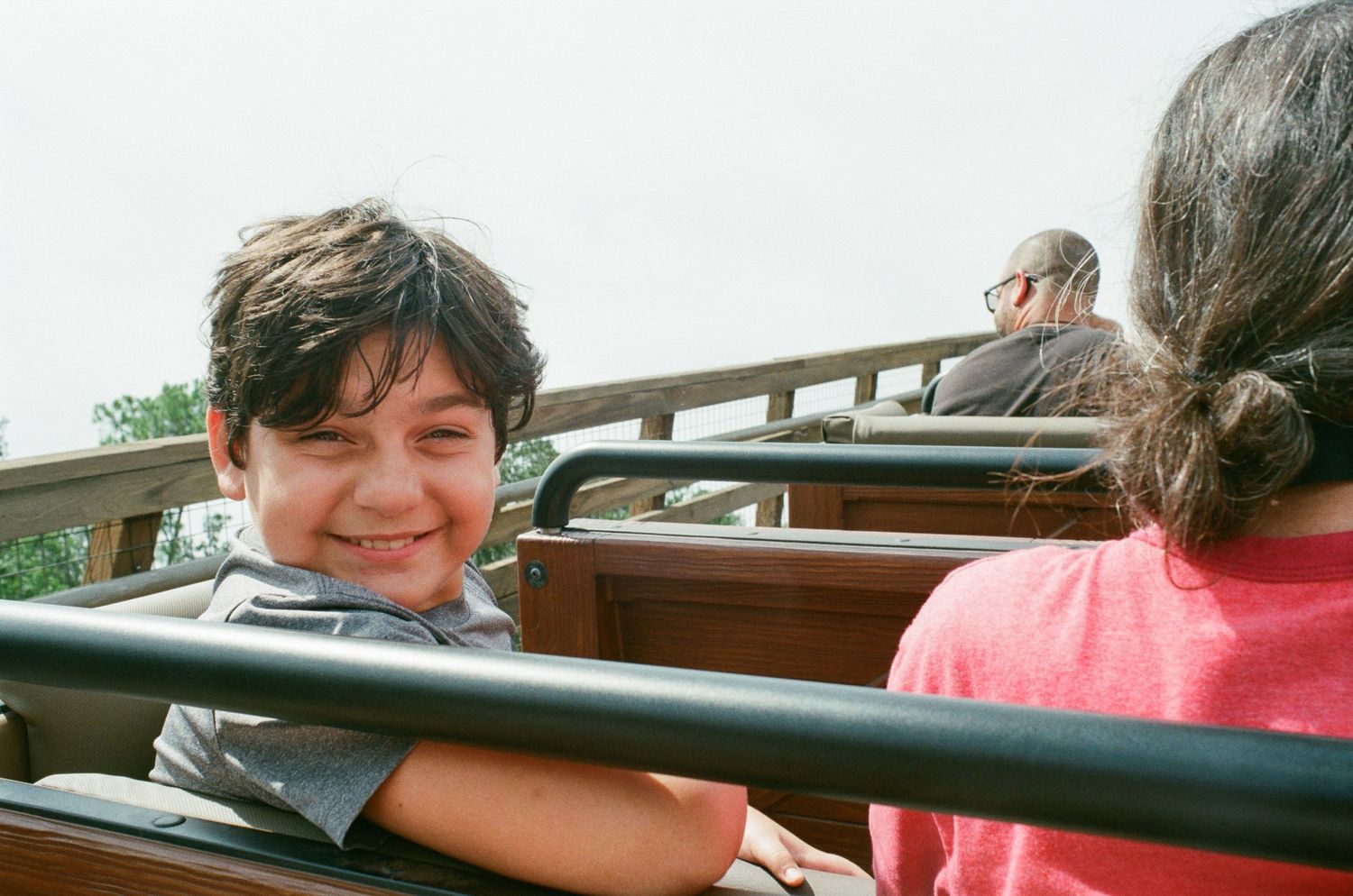 Smiling boy on an outdoor amusement park ride with other passengers visible in the background.